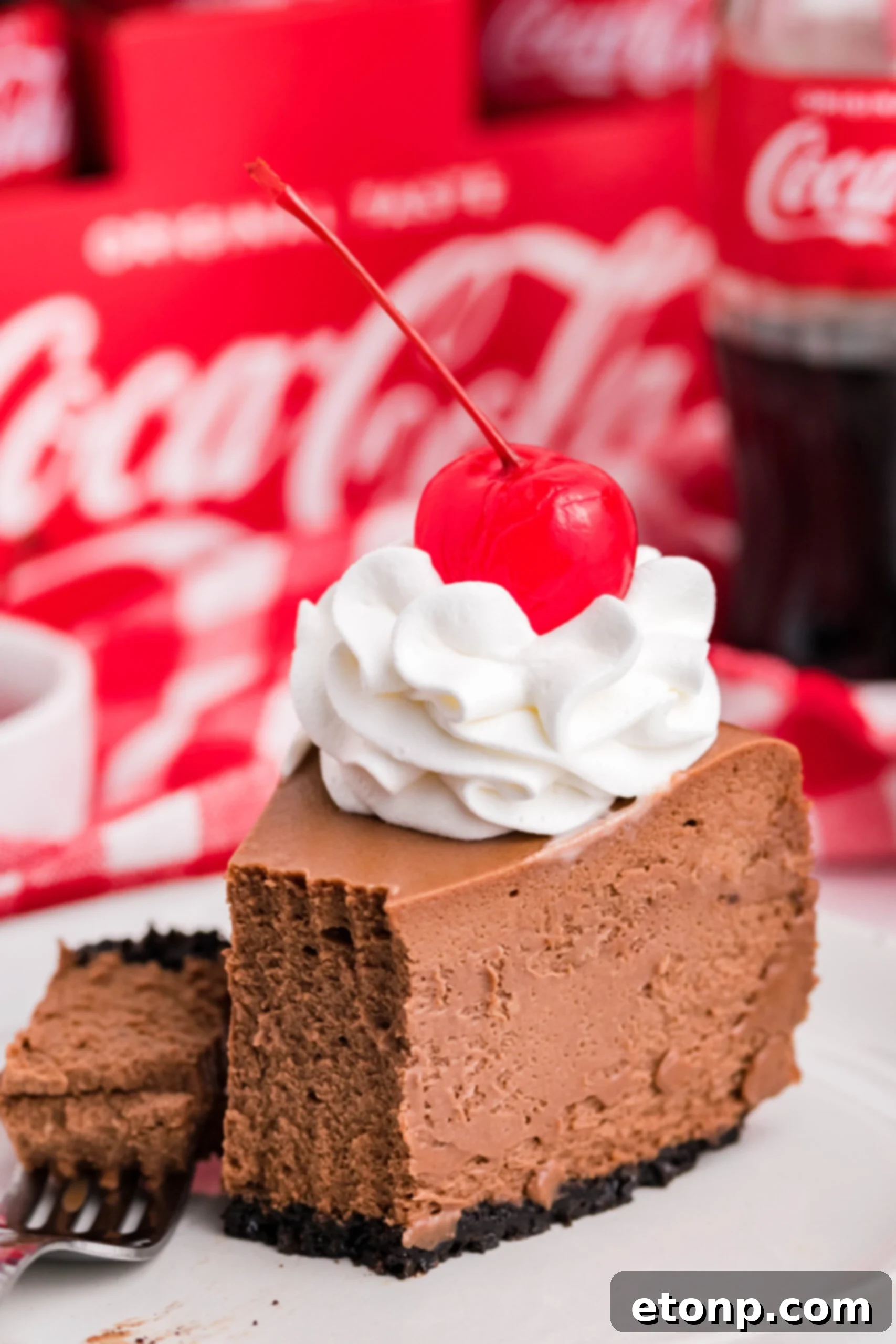 Decadent Coca-Cola Cheesecake 8 Side view of a slice of Coca Cola on a white dish with a piece removed and on a fork.