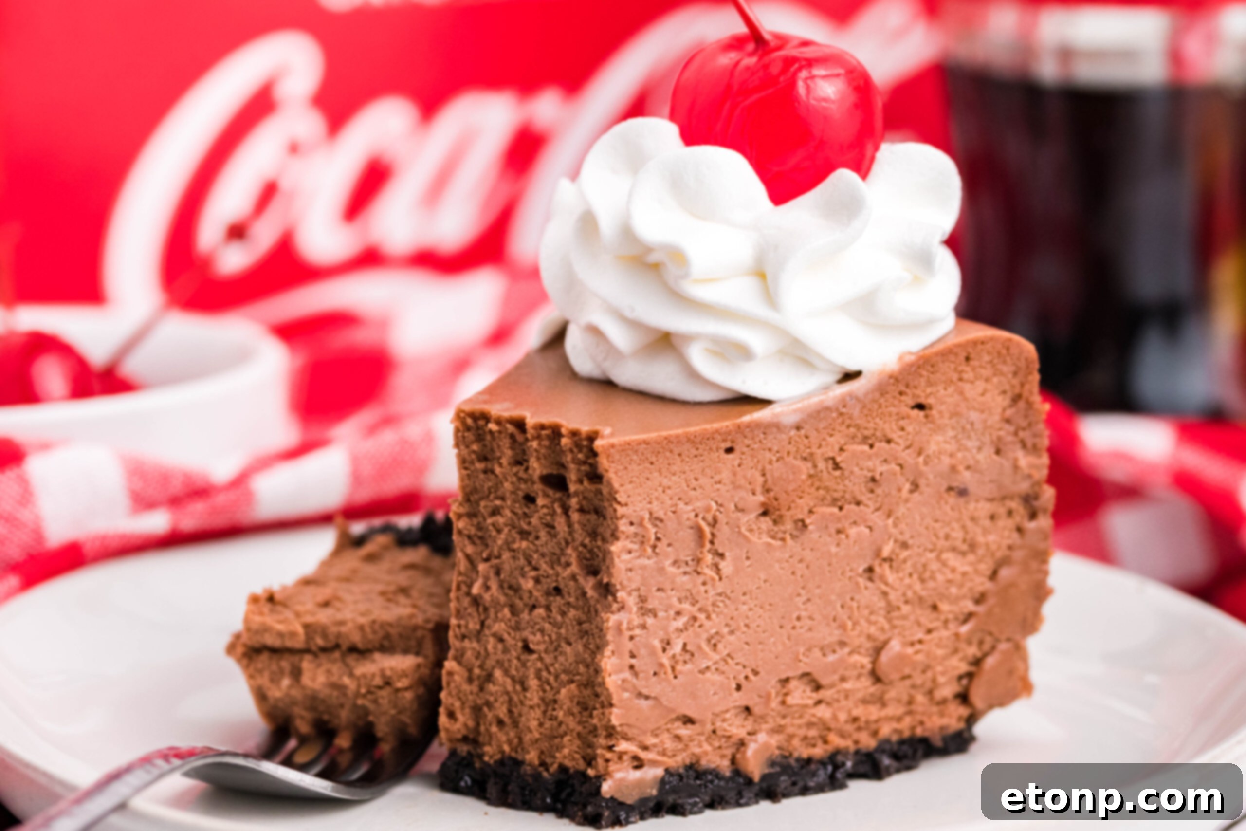 Decadent Coca-Cola Cheesecake 10 Side view of a slice of Coca Cola on a white dish with a piece removed and on a fork.