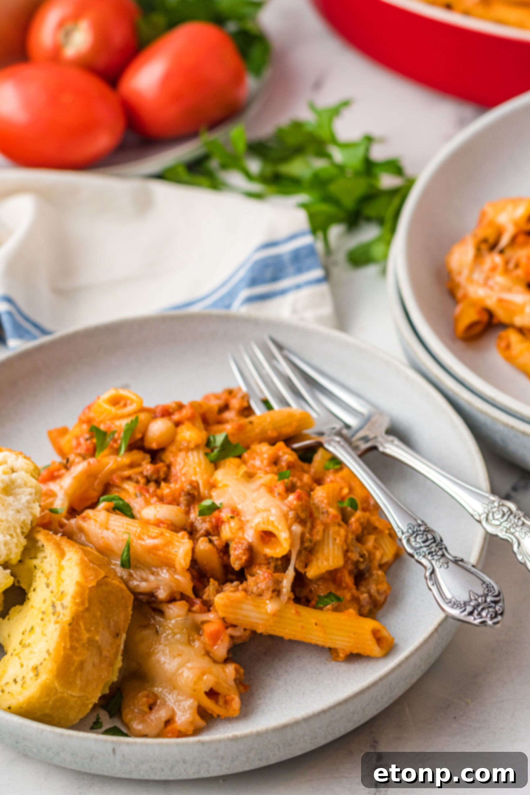 A single serving of Pasta Fagioli al Forno on a gray plate, accompanied by crisp garlic bread and silver cutlery.