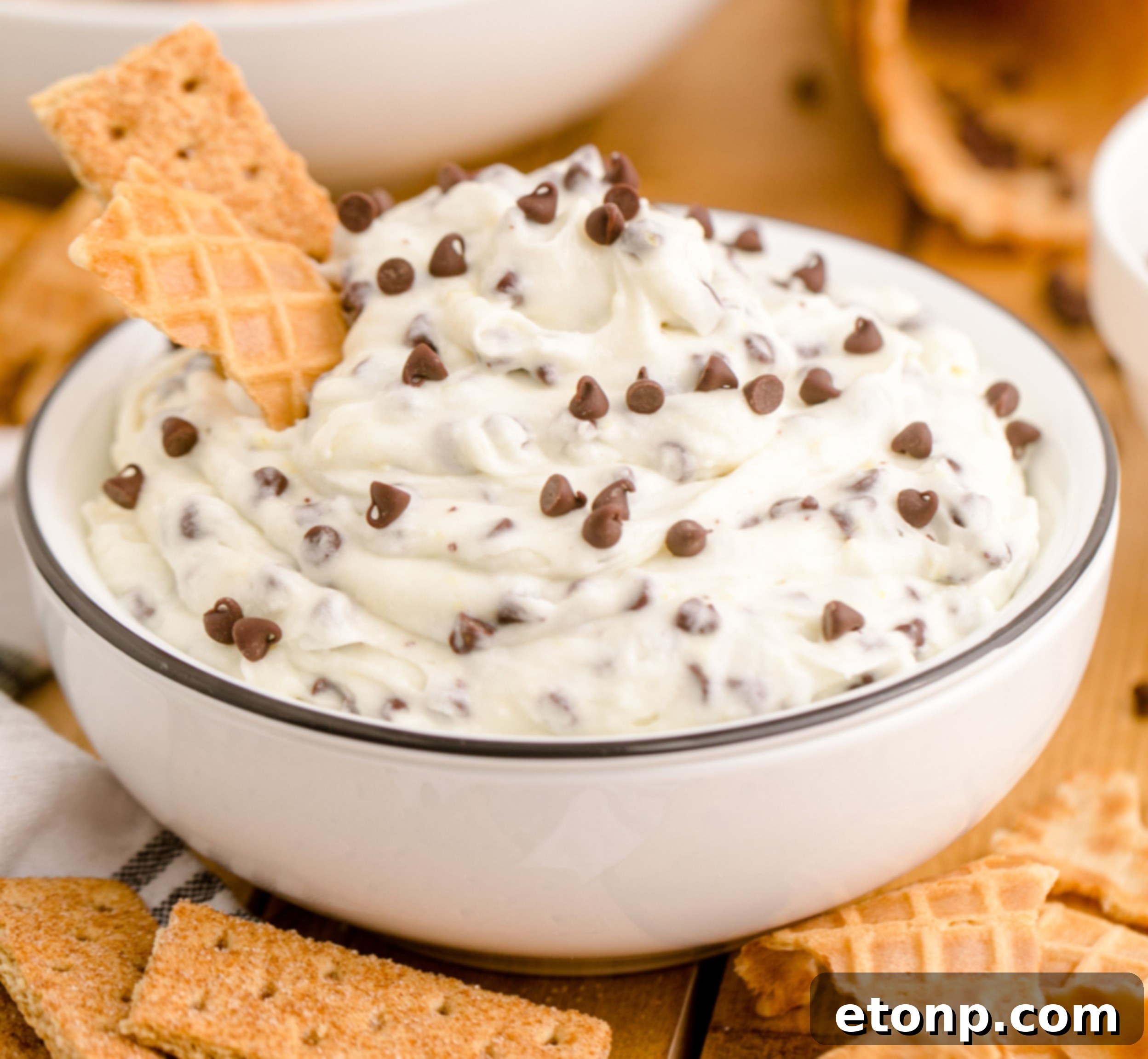 A vibrant, close-up shot of the creamy Cannoli Dip in a white dish, beautifully garnished with a piece of waffle cone, inviting a taste.