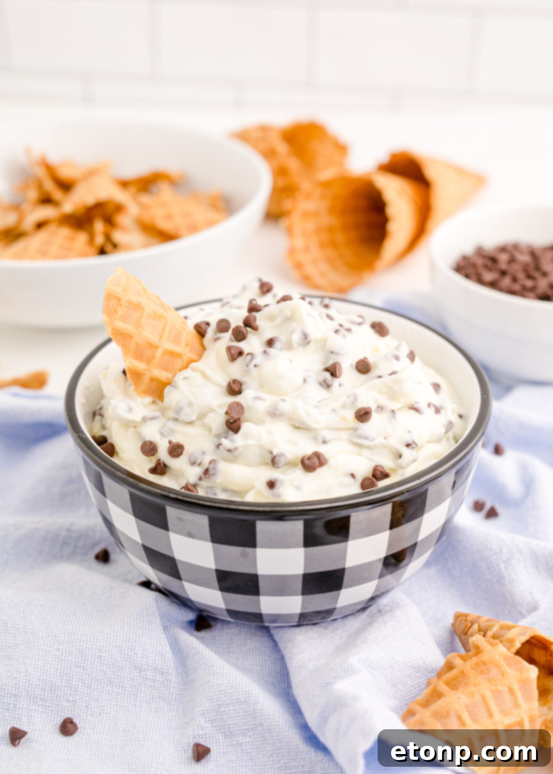 A stunning side view of the Cannoli Dip, beautifully presented in a black and white dish with a piece of waffle cone, emphasizing its inviting texture.