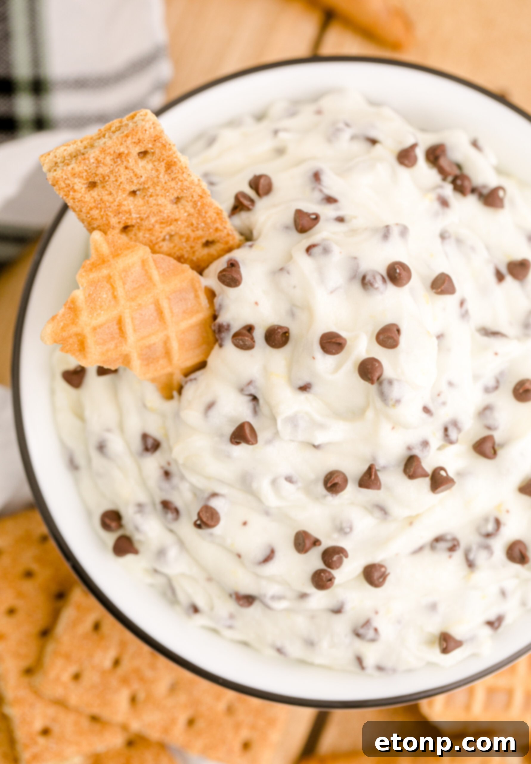 An inviting, close-up overhead view of the Cannoli Dip in a black and white dish, served with both a waffle cone piece and a graham cracker, illustrating versatile dipping options.