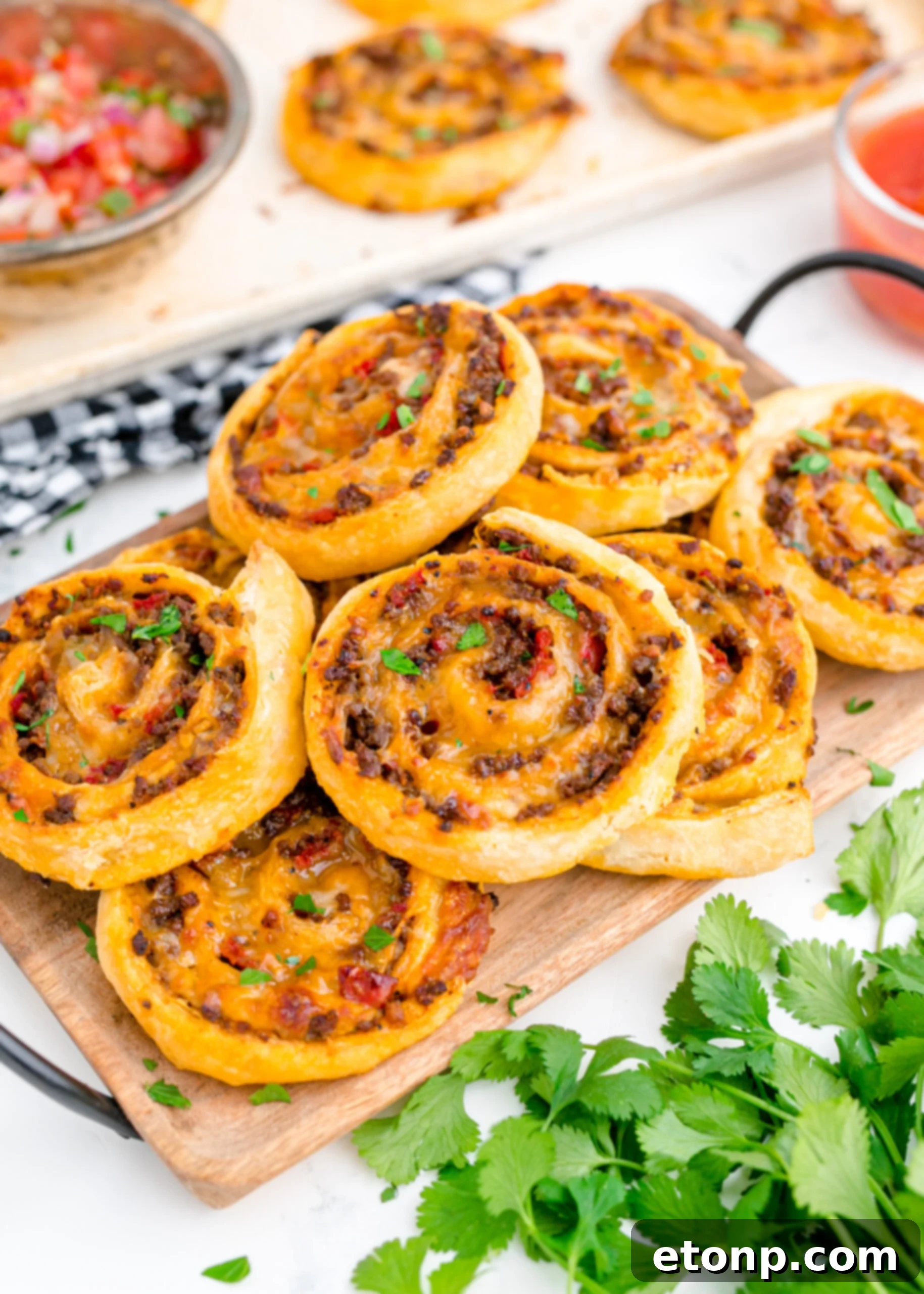 Side view of golden-brown Taco Pinwheels stacked on a rustic wooden cutting board, showcasing their flaky pastry and savory filling.