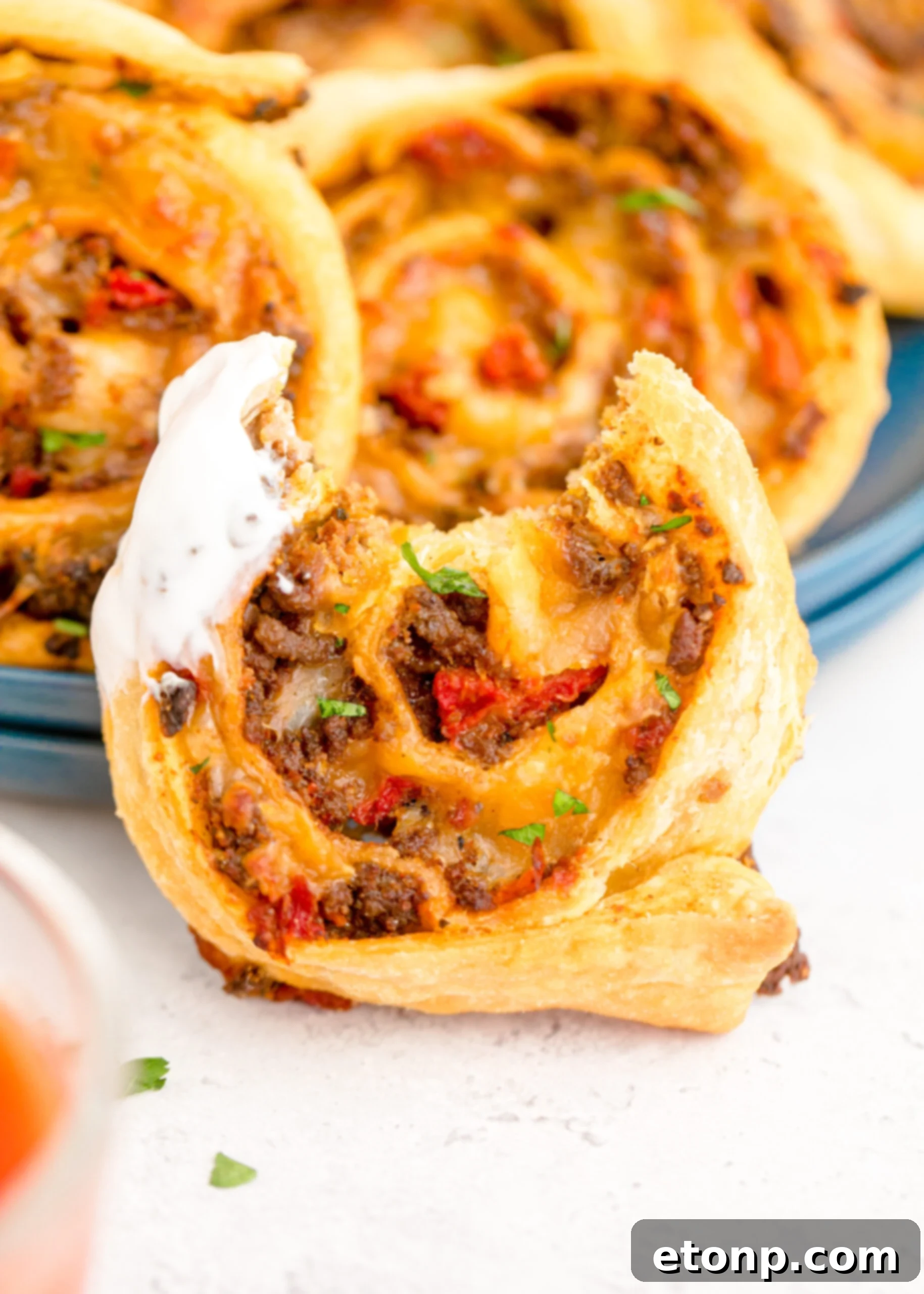 An inviting close-up of a propped-up Taco Pinwheel, revealing a bite taken out, with a side of creamy ranch dressing, suggesting it's ready to be savored.