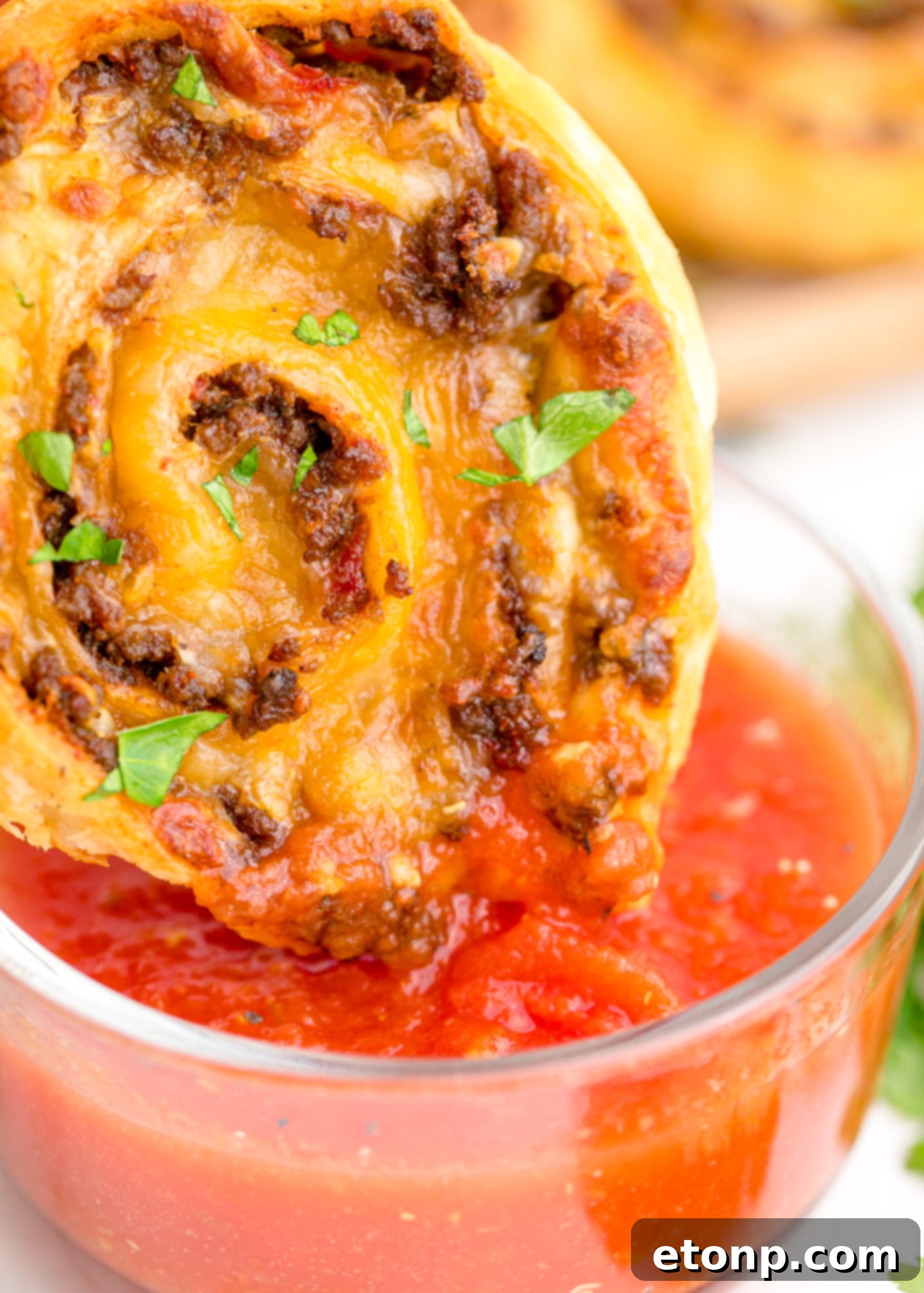 A close-up view of a crispy Taco Pinwheel being dipped into a clear bowl brimming with vibrant red salsa, ready to be enjoyed.