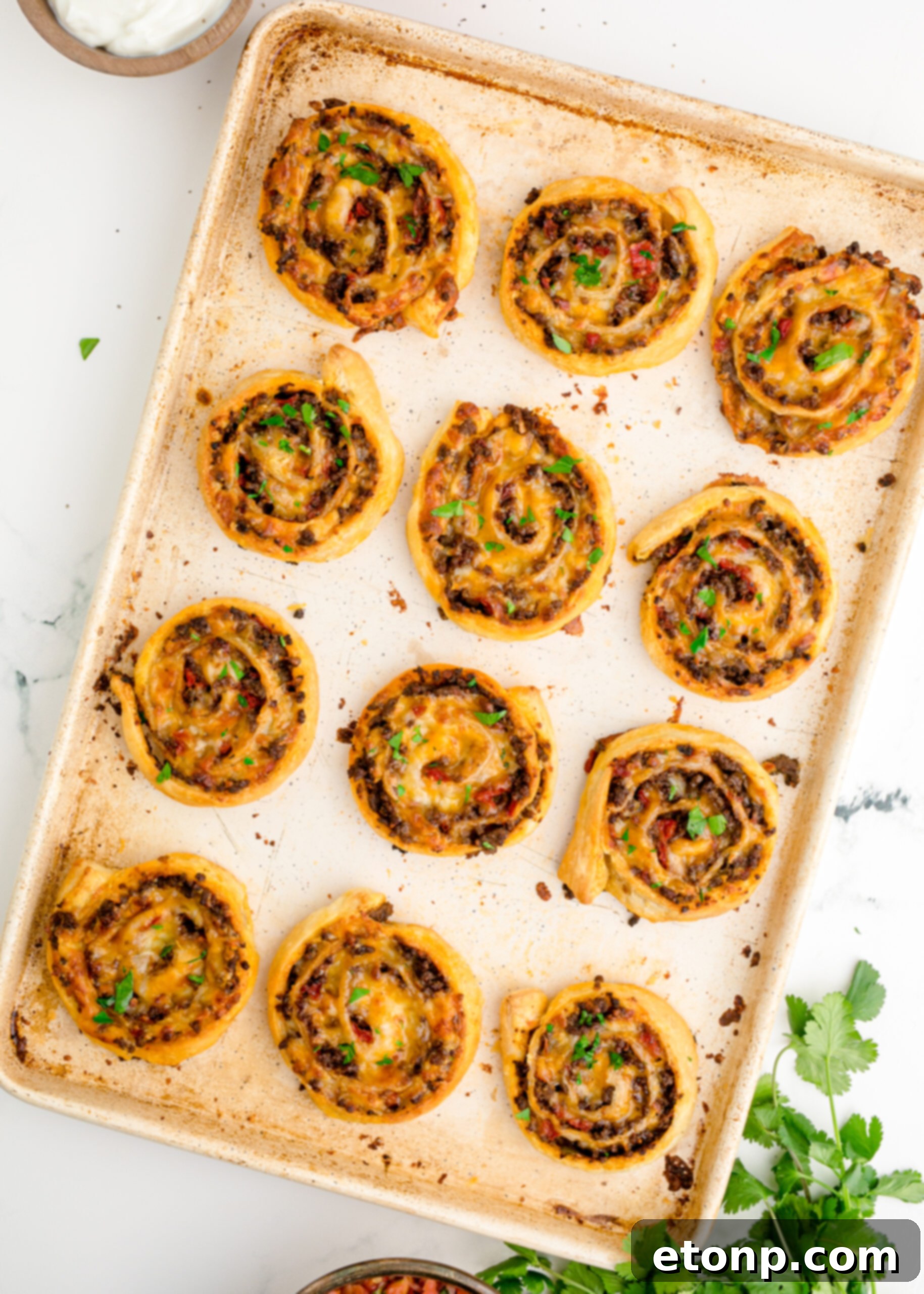 An appetizing overhead shot of multiple Taco Pinwheels neatly arranged on a baking sheet, showcasing their golden-brown finish.
