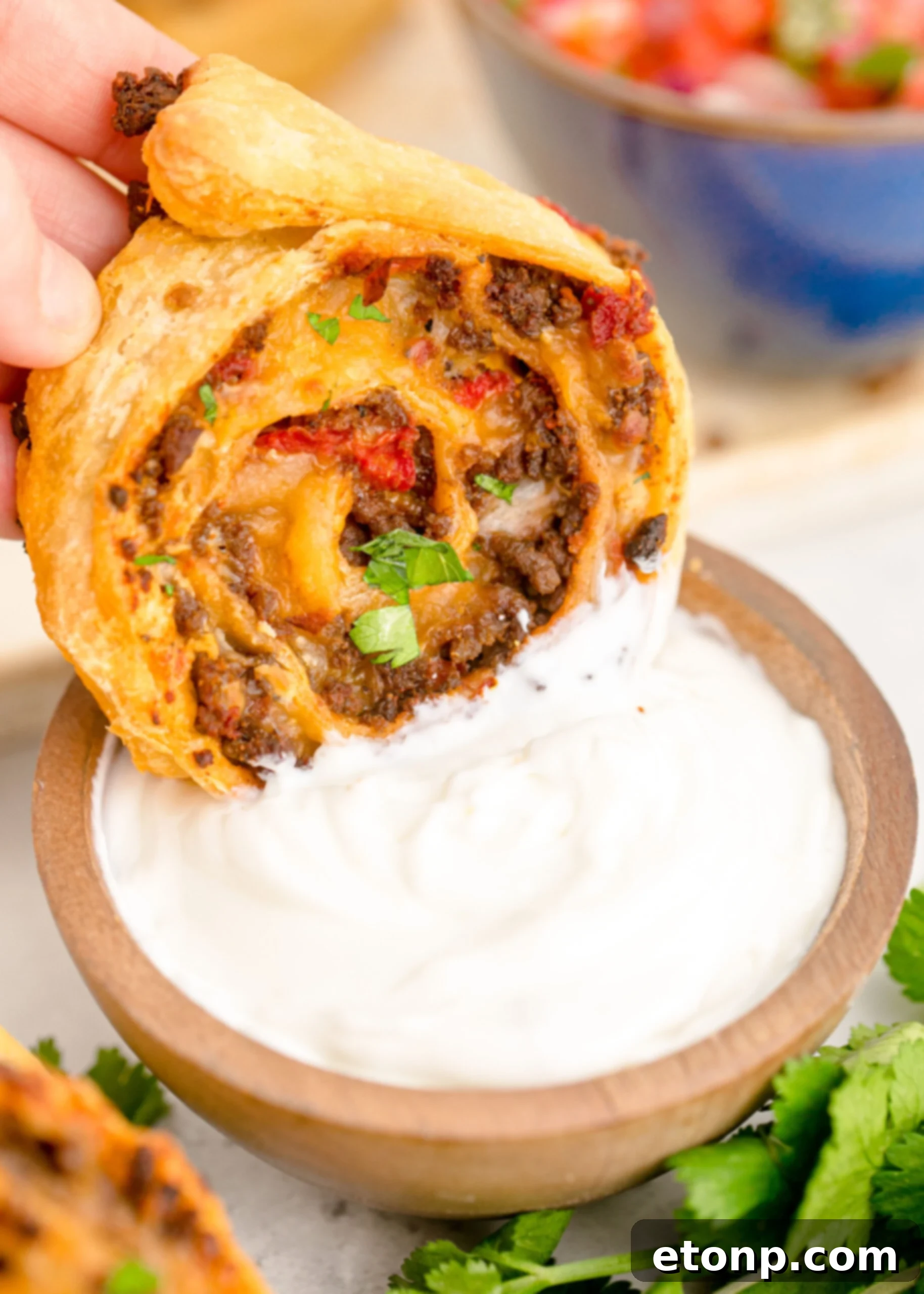Close-up of a Taco Pinwheel being dipped into a small wooden bowl filled with creamy ranch dressing, highlighting the contrast.