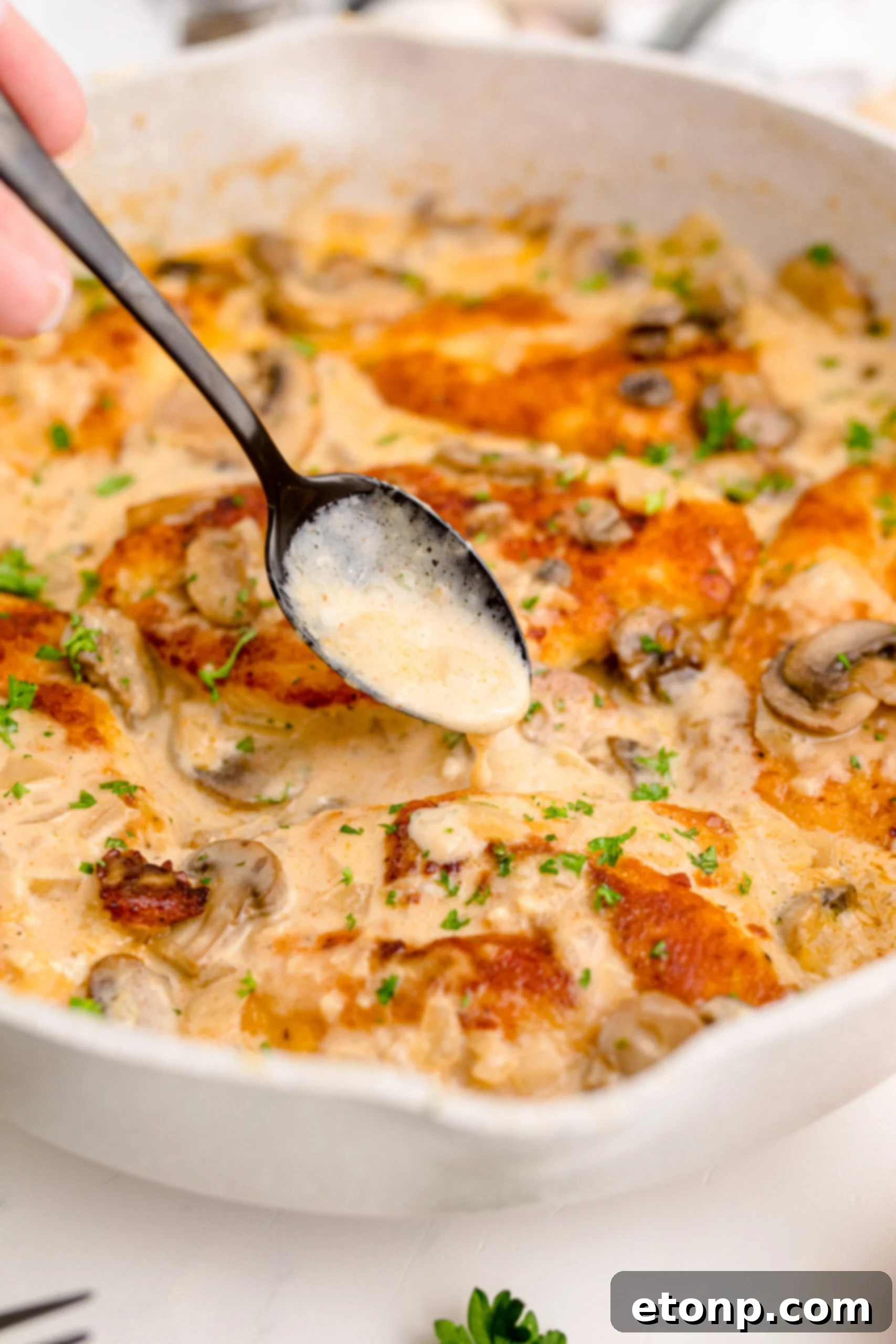 Chicken Marsala in a white skillet with a spoon pouring sauce over a piece of chicken 
