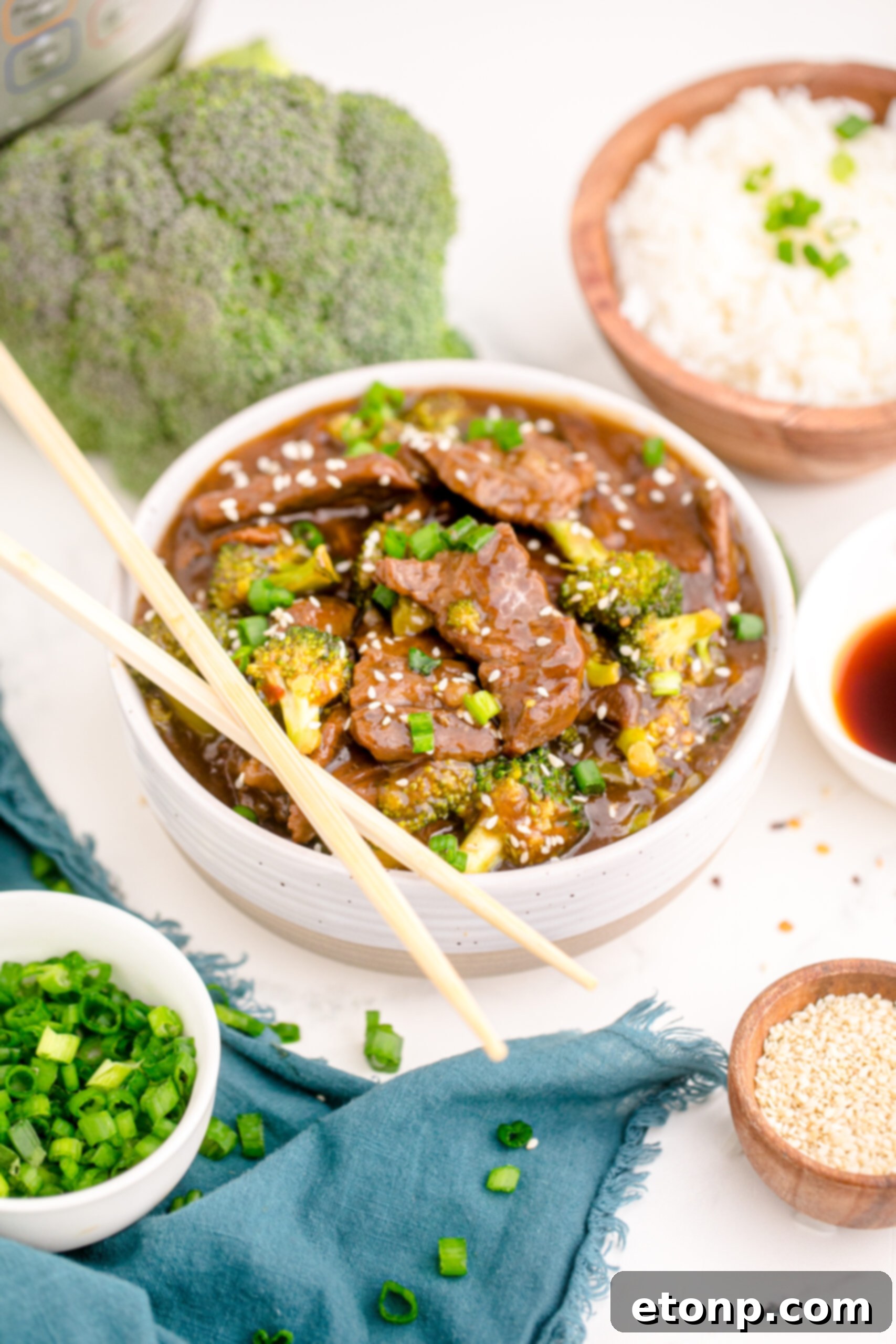 Side view of a bowl of Instant Pot Beef and Broccoli with a pair of elegant chopsticks resting on the rim, inviting you to enjoy the meal.