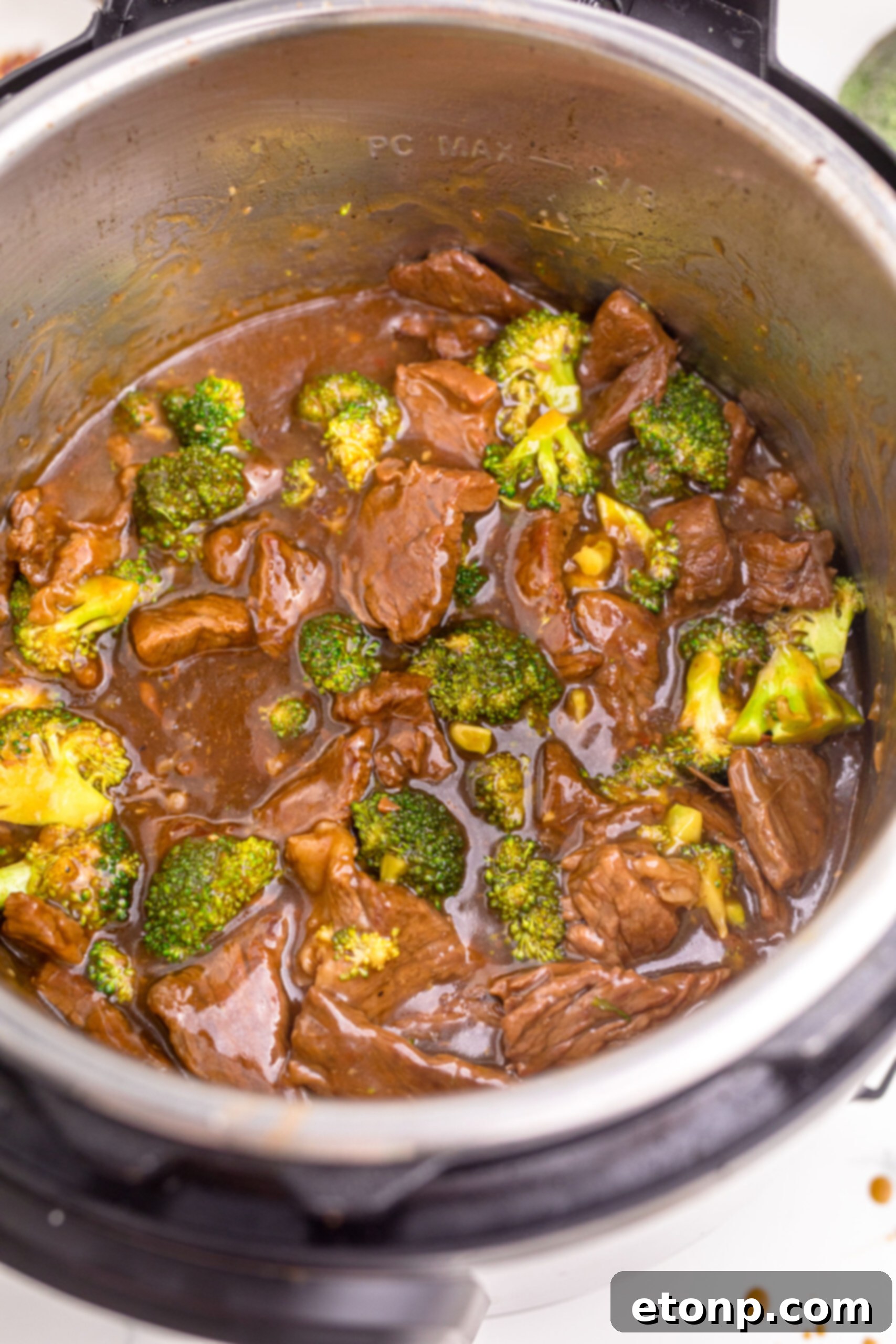 Instant Pot Beef and Broccoli cooking inside the Instant Pot, with some food lifted by a spoon, showcasing its rich sauce and inviting appearance.
