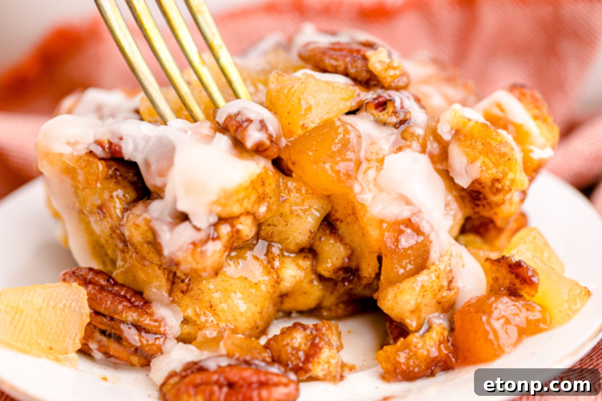 A bite of Cinnamon Roll Casserole being taken with a gold fork from a white plate, emphasizing its delightful texture and glaze.