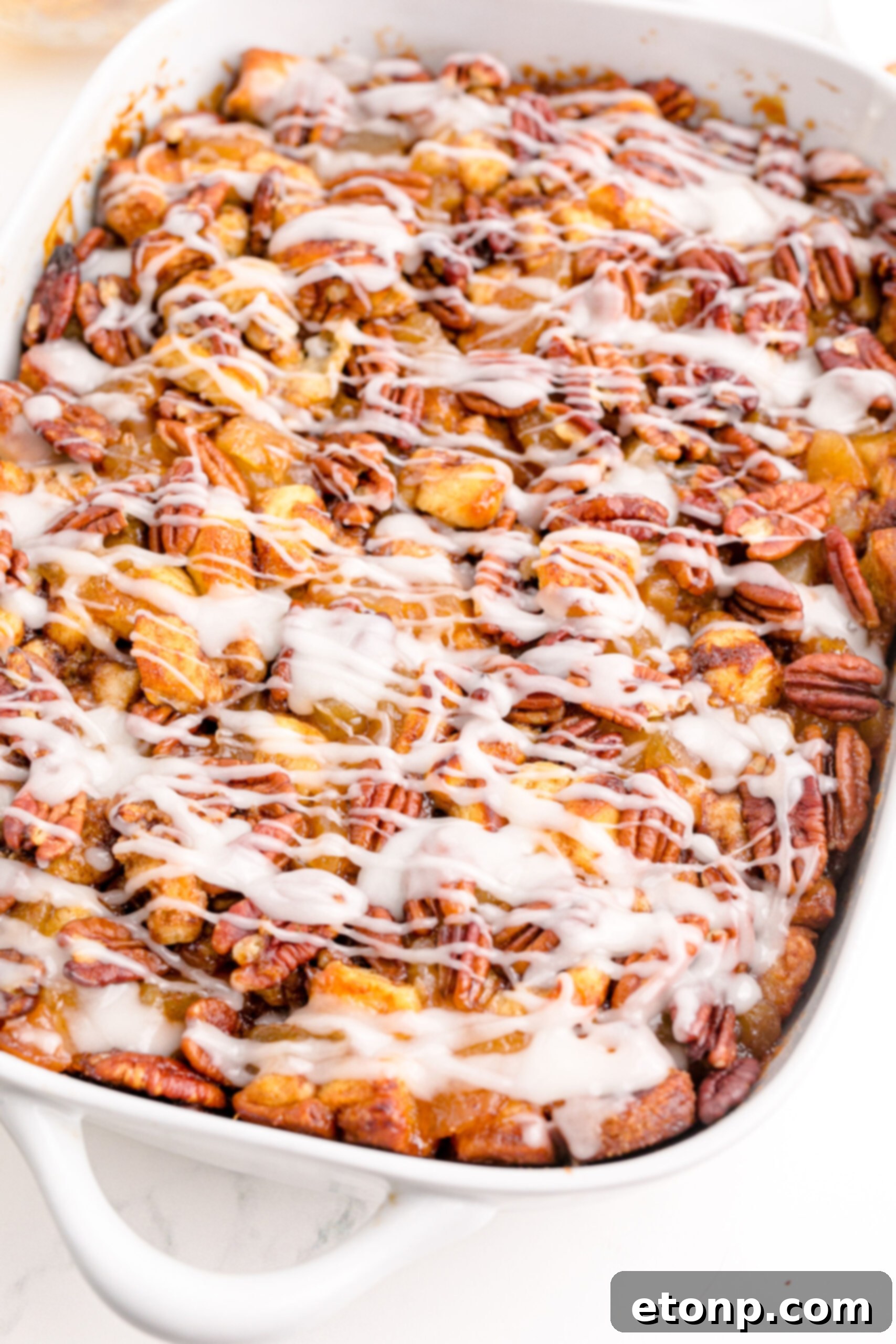 The Cinnamon Roll Casserole, glistening with melted icing, is showcased in a white baking dish, fresh out of the oven.
