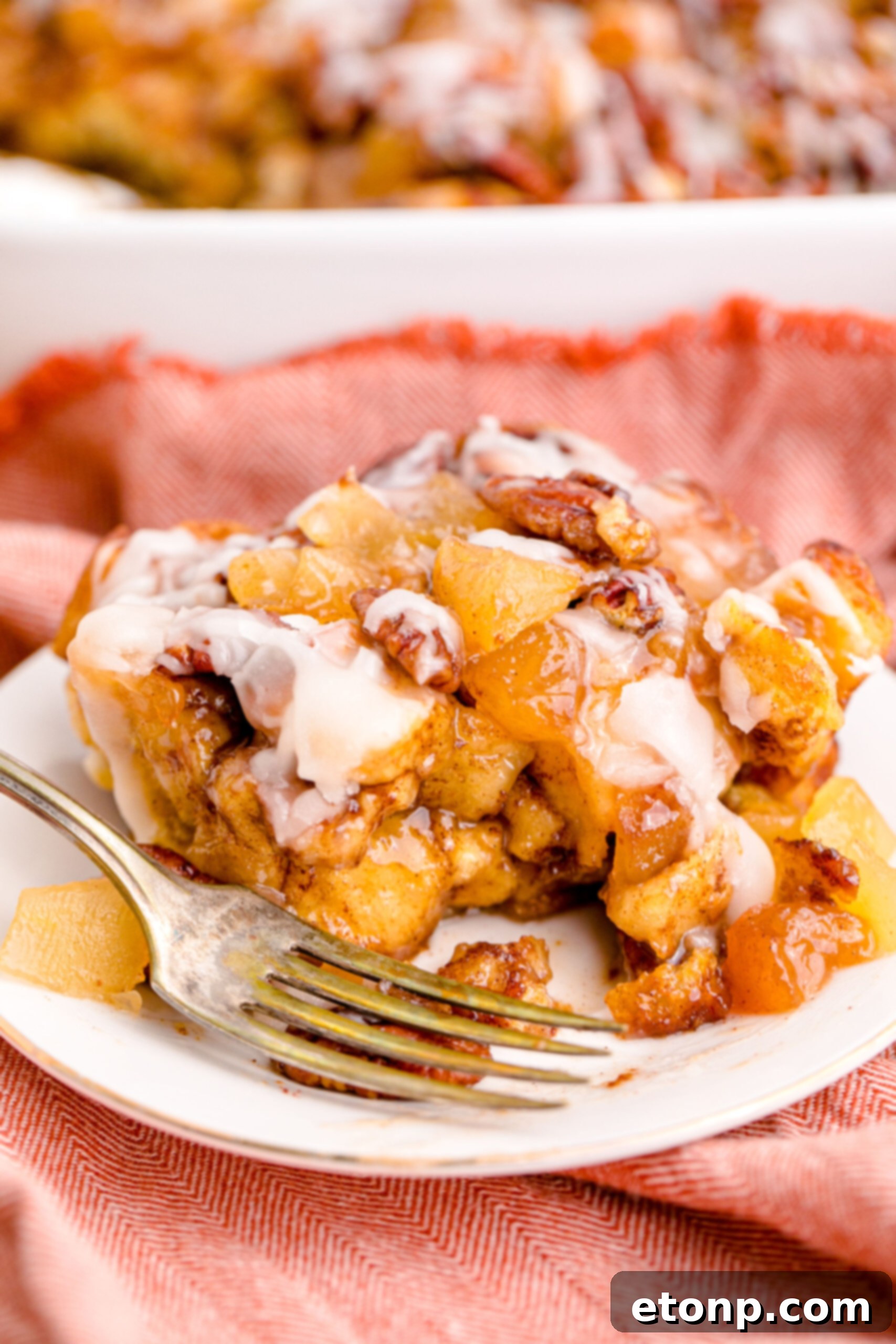 A close-up shot of a bite being removed from the Cinnamon Roll Casserole on a white plate with a gold fork, highlighting its rich textures.