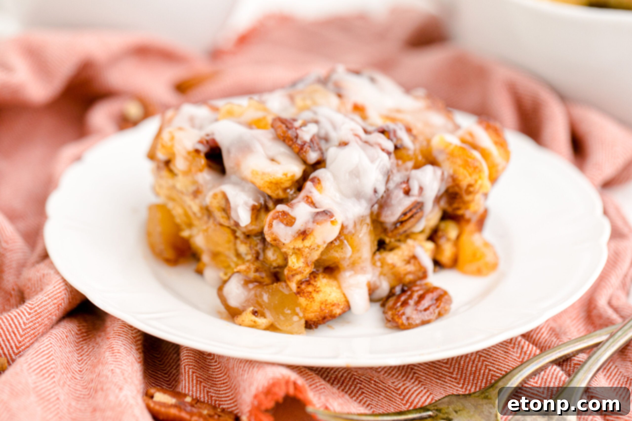 A generous serving of Cinnamon Roll Casserole, lavishly covered in white icing, presented beautifully on a white plate.