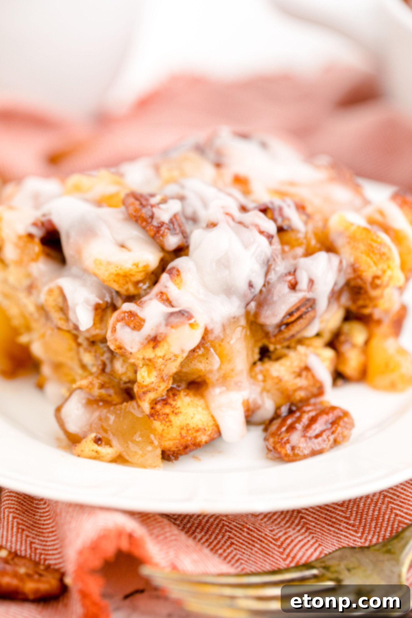 A freshly baked Cinnamon Roll Casserole, generously topped with sweet white icing, rests on a white dish, ready to be served.