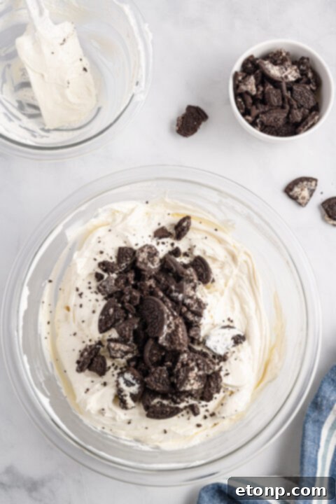 No-Bake Oreo Cheesecake Magic 11 A close view of the top of the No Bake Oreo Cheesecake, adorned with whipped cream and Oreo pieces.