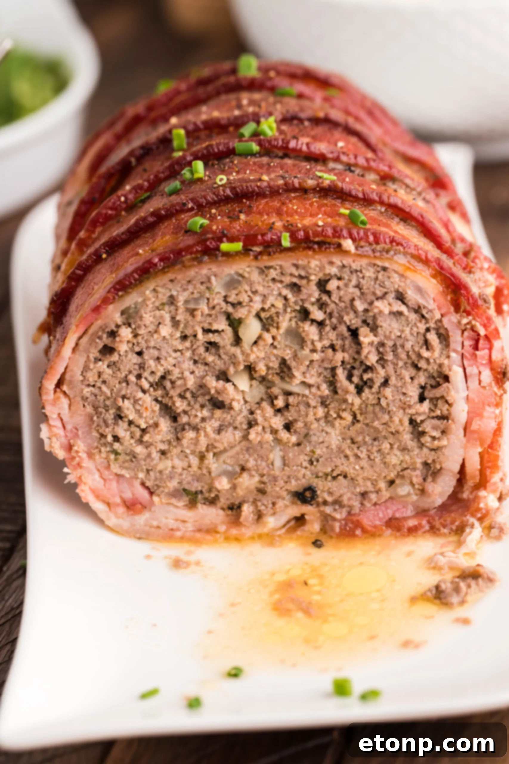 Bacon-Cloaked Meatloaf 3 Front view of Bacon Wrapped Meatloaf on a white serving dish.