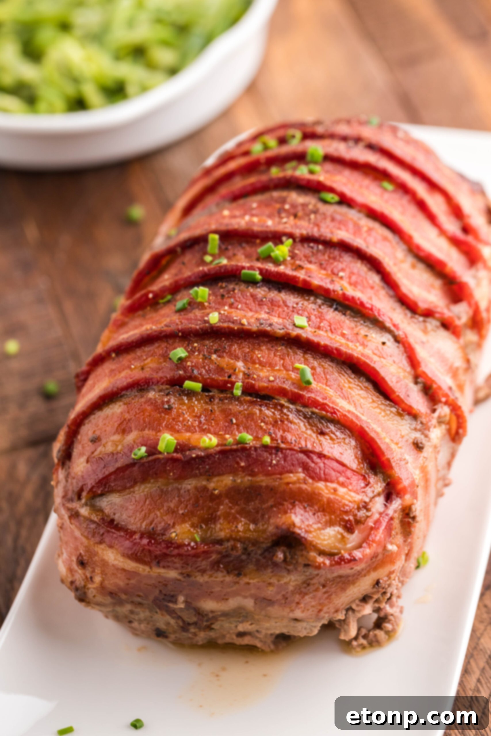 Bacon-Cloaked Meatloaf 4 View of Bacon Wrapped Meatloaf on a white serving dish.