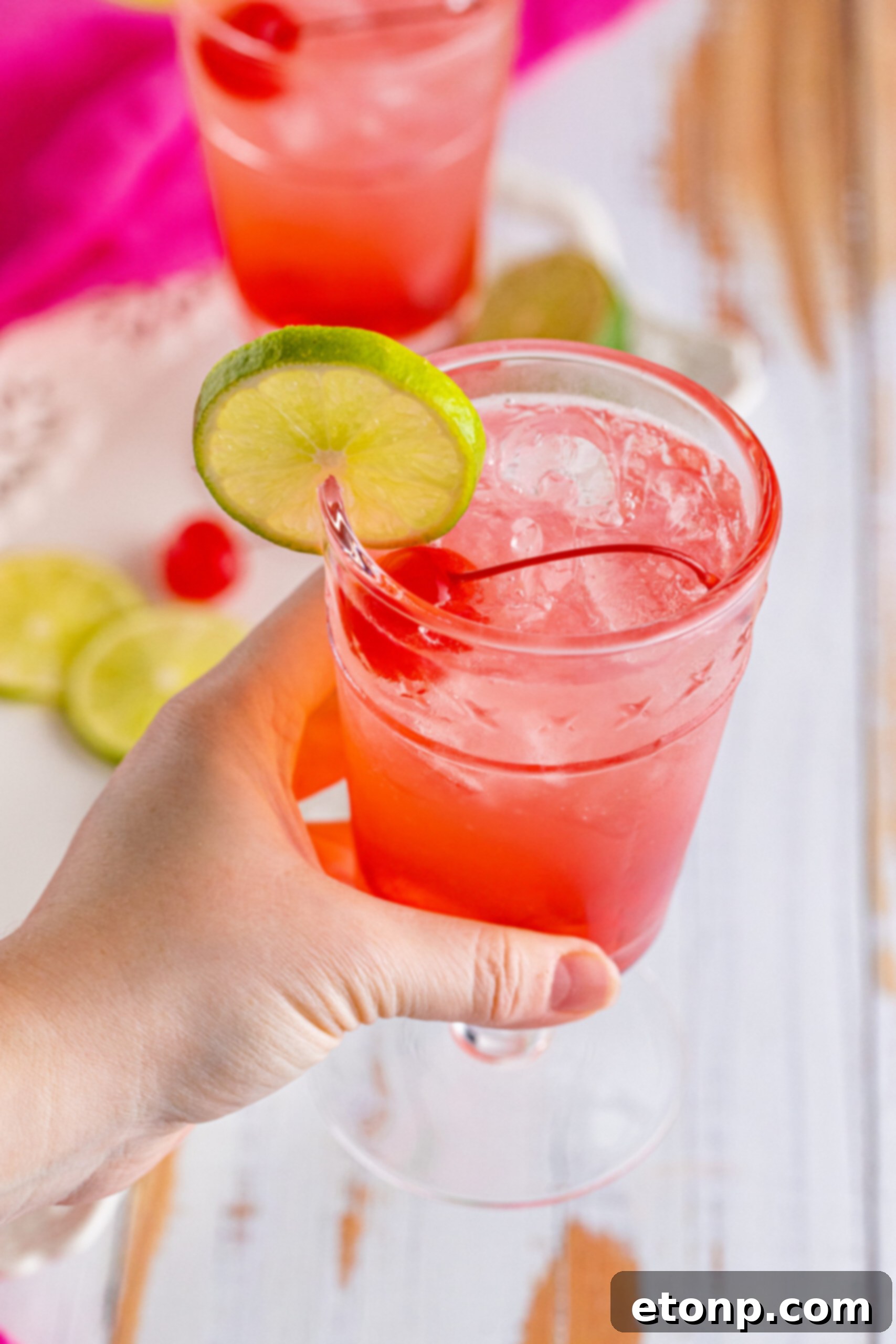 45 degree view of Dirty Shirley Temple garnished with a lime slice being held.