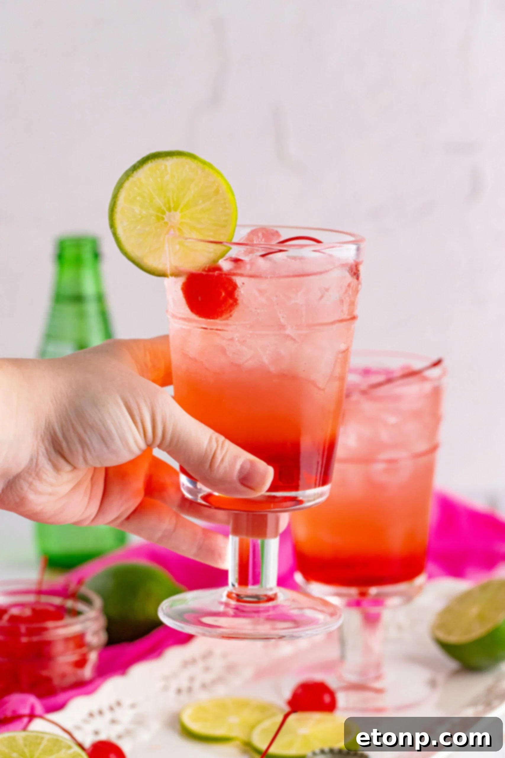 Side view of Dirty Shirley Temple garnished with a lime slice being held.
