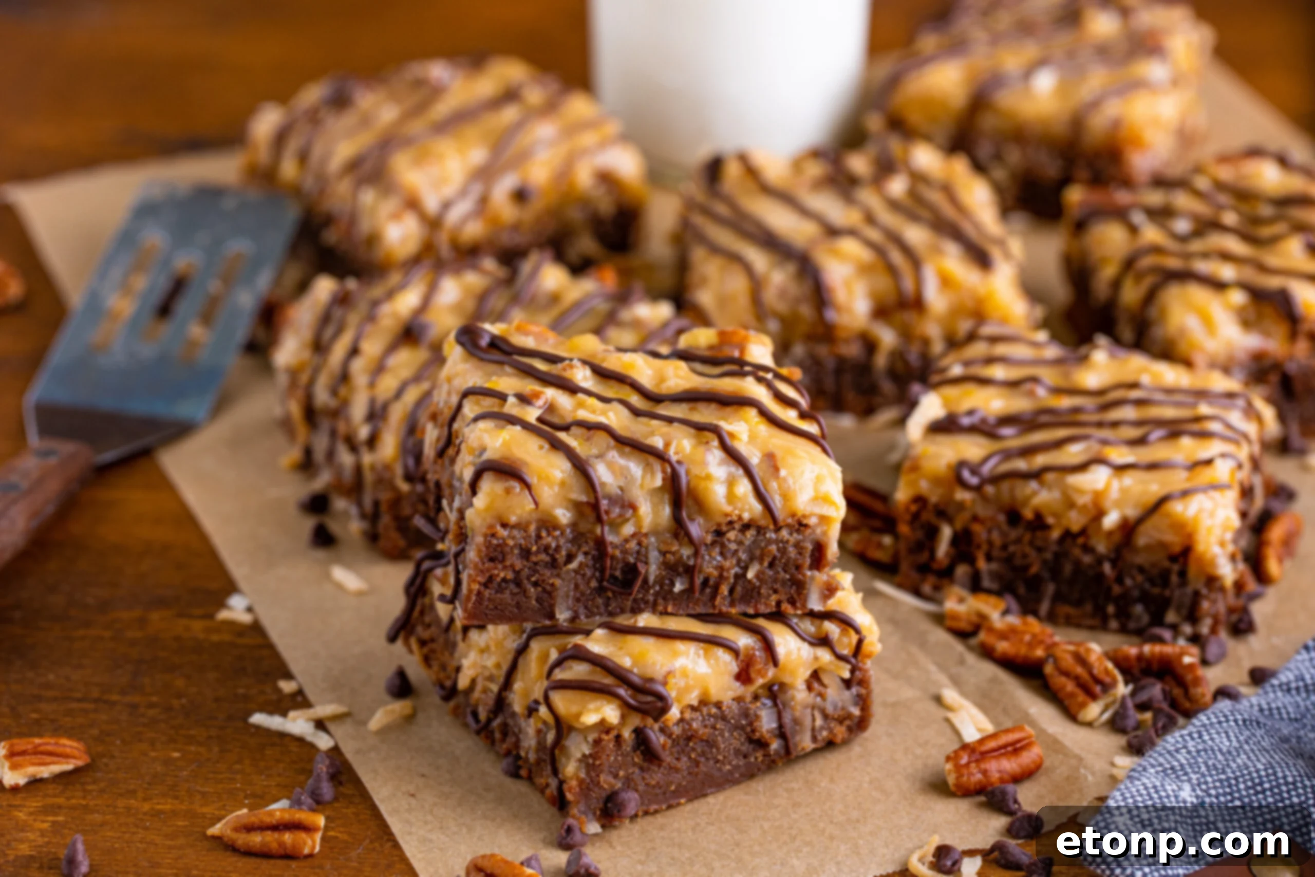 German Chocolate Brownies arranged on a wood table, complemented by scattered chopped pecans and chocolate chips.