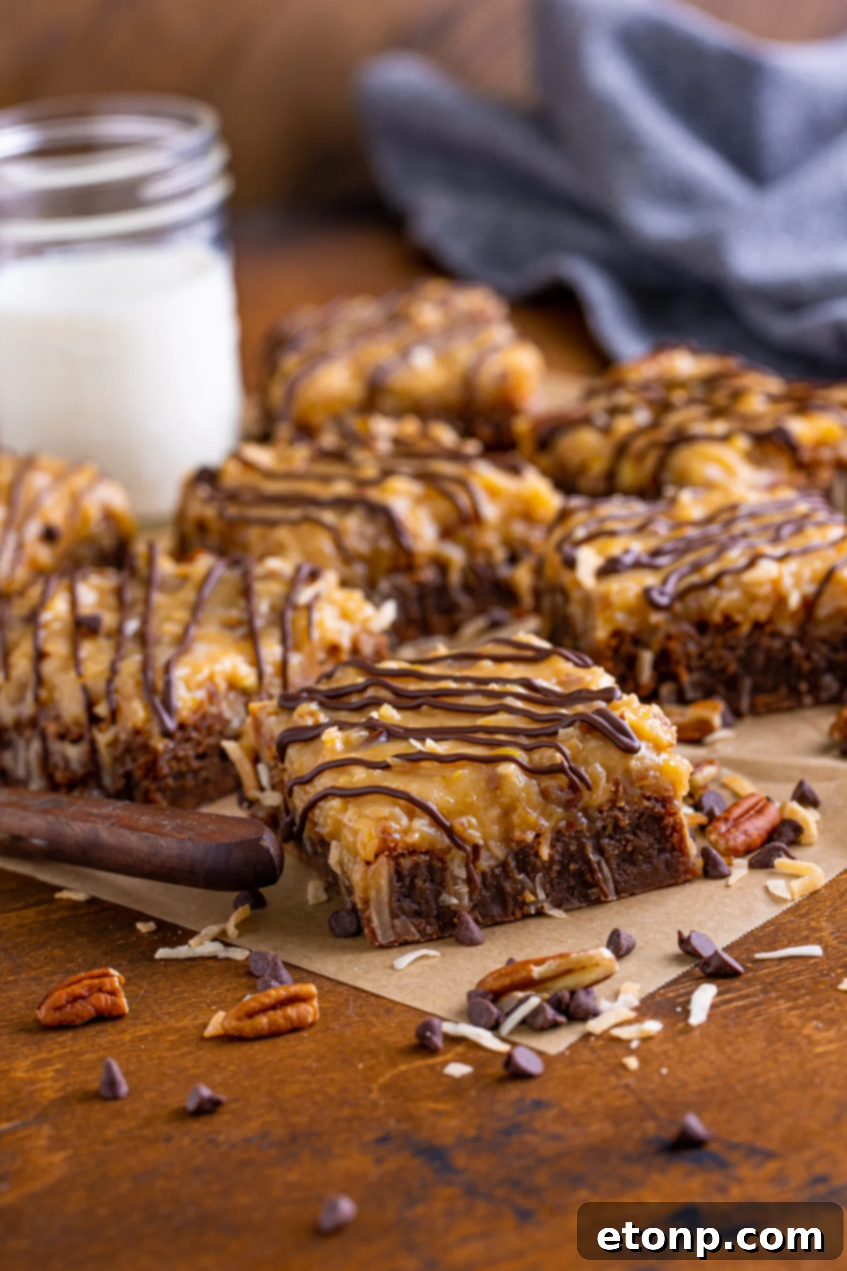 Side view of several German Chocolate Brownies displayed on parchment paper, showing the thick layer of coconut-pecan frosting.