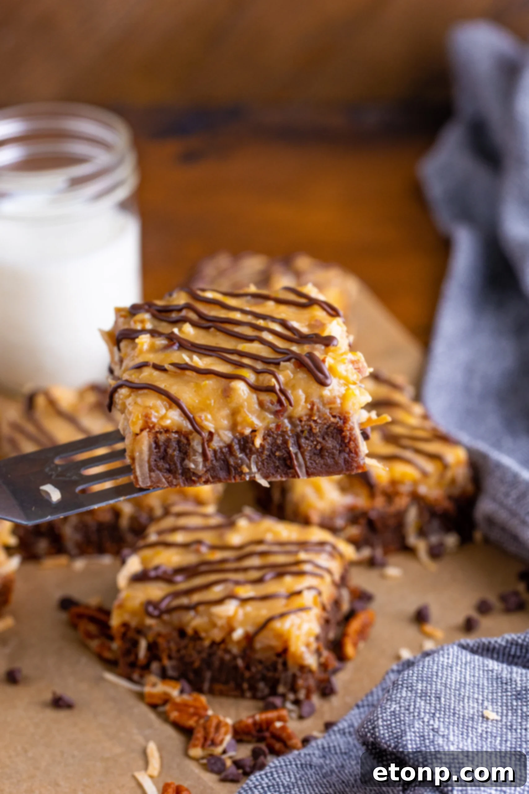 Front view of a single German Chocolate Brownie resting on a silver spatula, showing its perfect square shape and generous topping.