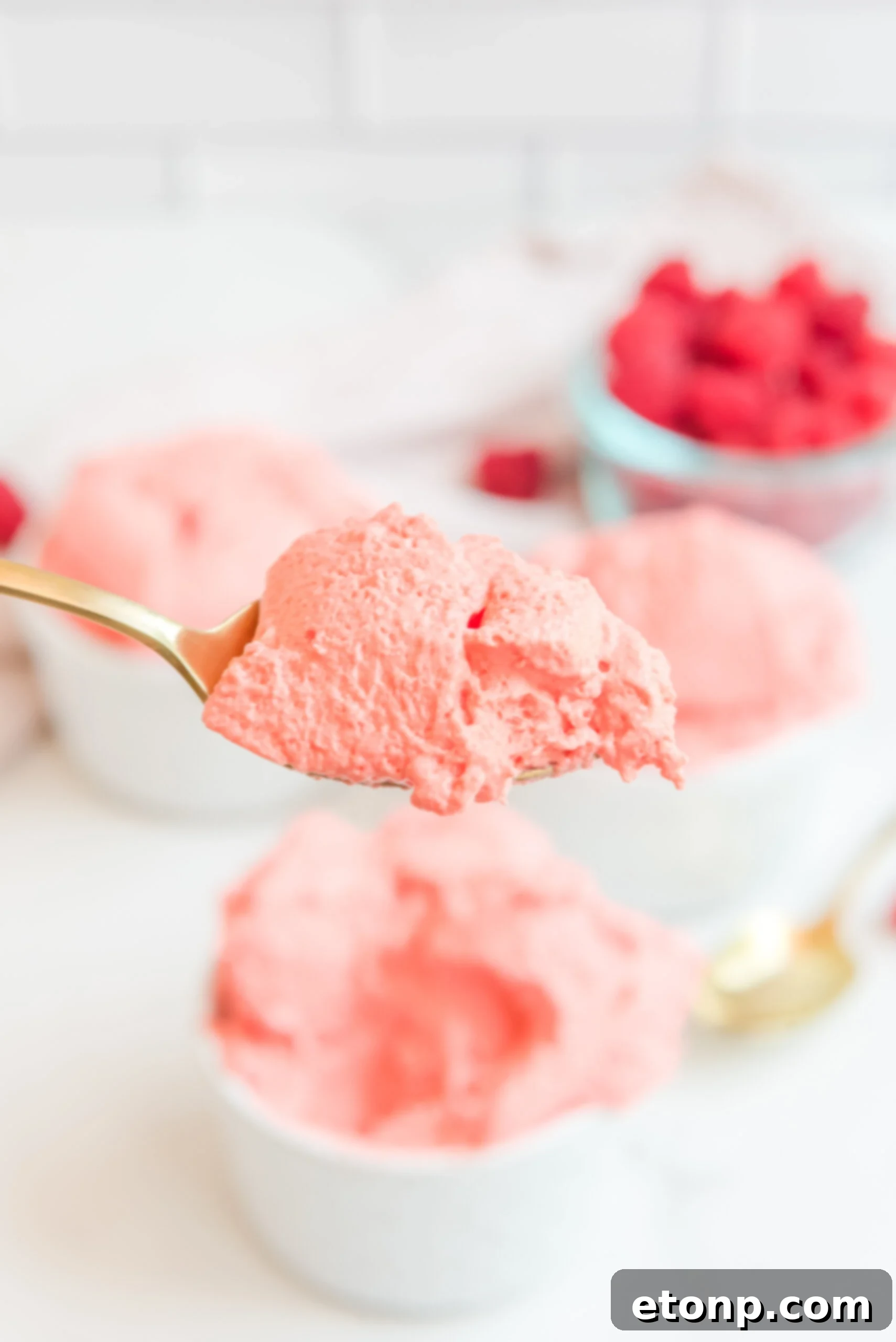 A gold spoon brimming with a perfect spoonful of Raspberry Jello Fluff, ready to be enjoyed, highlighting its smooth and creamy texture.