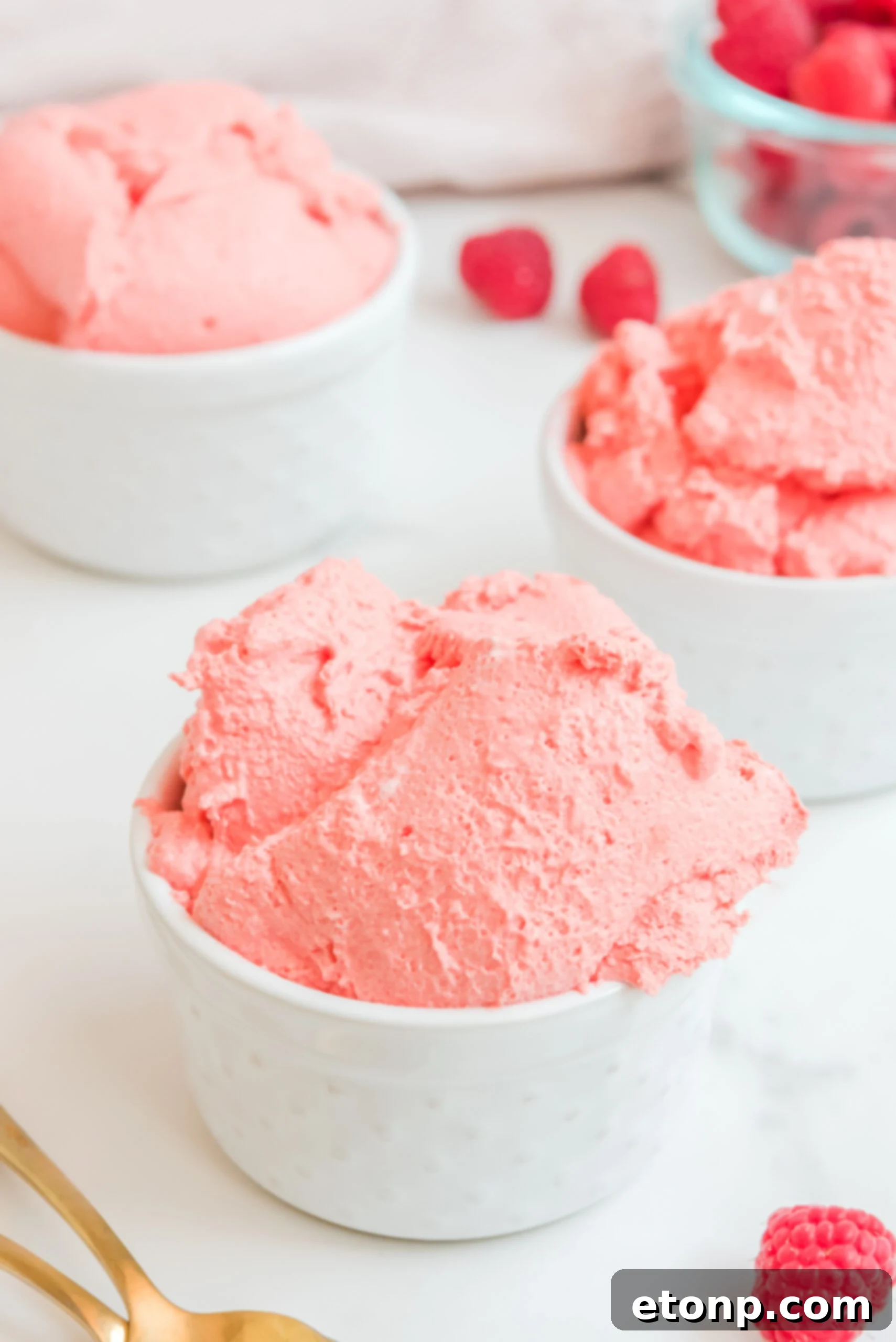 Close-up front view of Raspberry Jello Fluff in a white dish, garnished with a swirl of whipped cream and a single fresh raspberry, highlighting its fluffy texture.