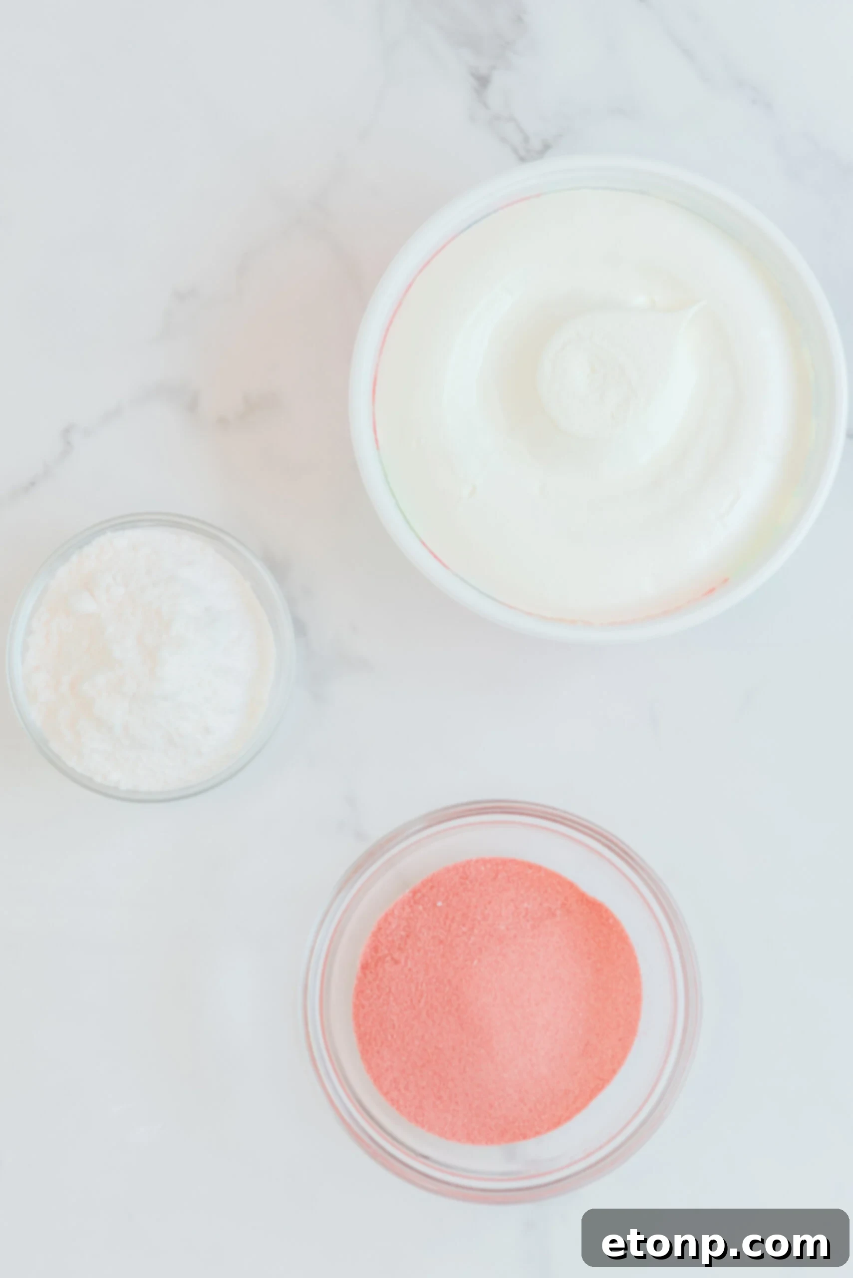 Overhead view of the four main ingredients needed to prepare Raspberry Jello Fluff: a packet of raspberry Jello, instant vanilla pudding mix, a tub of whipped topping, and two measuring cups of water.