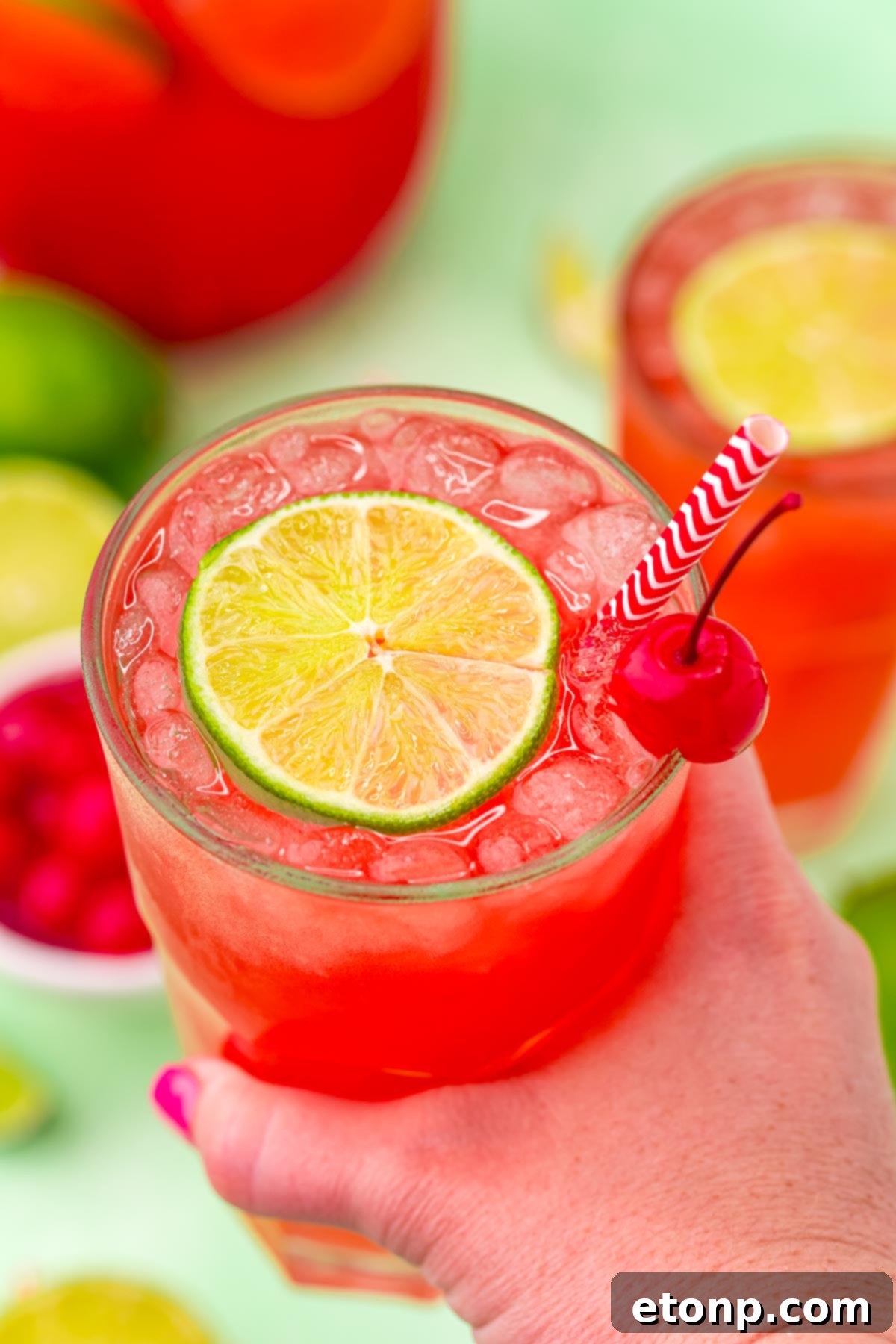 45 degree view of Cherry Limeade being held and garnished with a lime and cherry.
