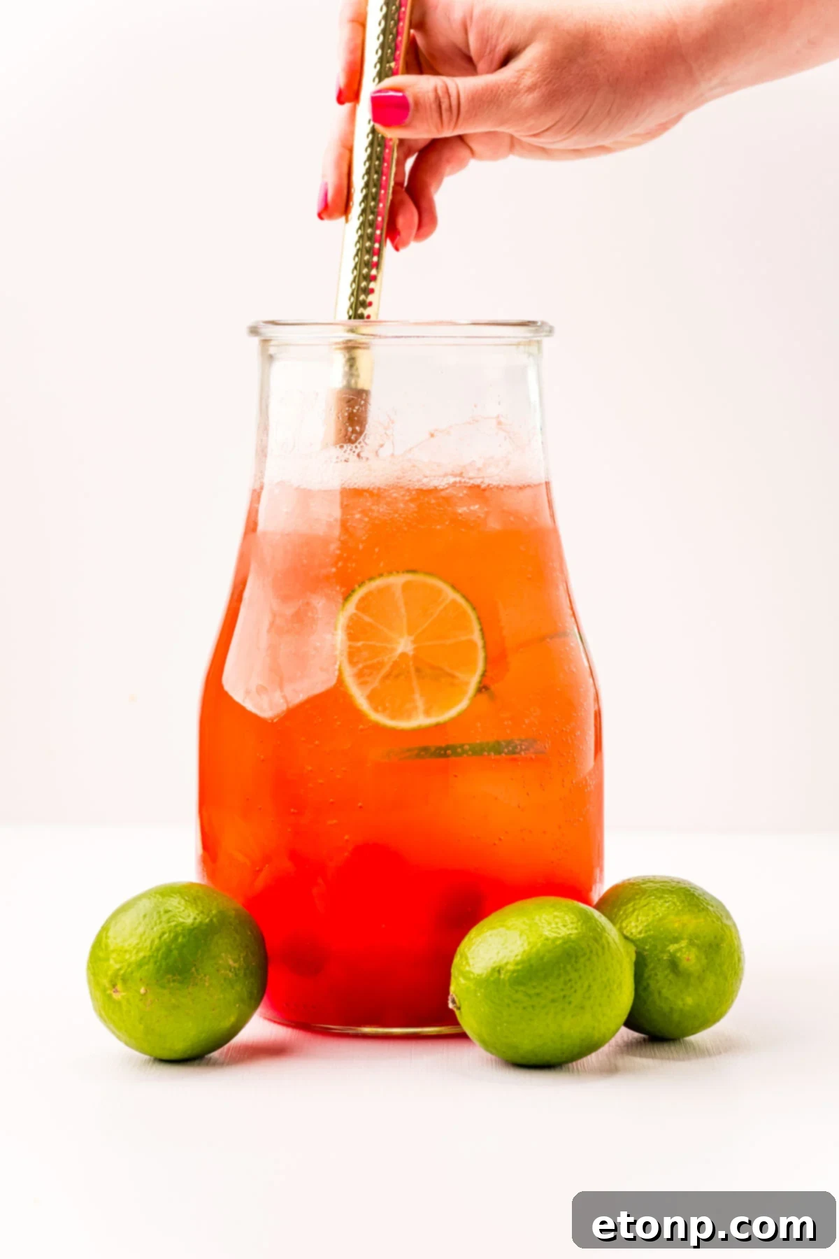 Front view of Cherry Limeade in a glass pitcher surrounded by whole limes.