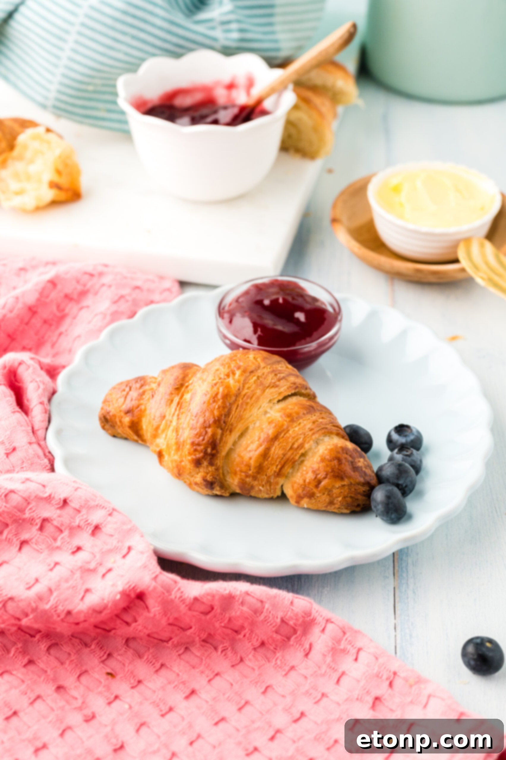 Front view of Homemade Croissants served on a white dish with jam and fresh blueberries.