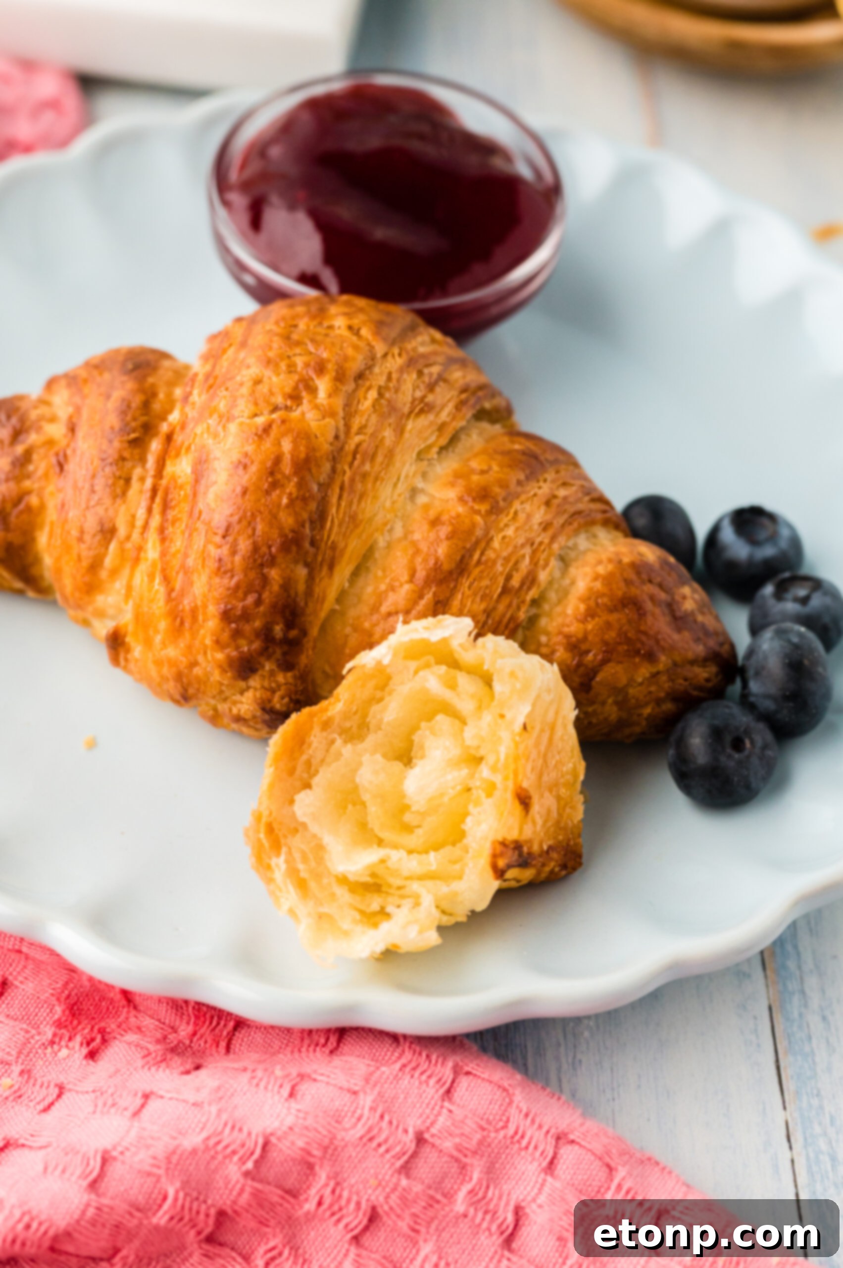 Front view of Homemade Croissants served on a white dish with jam and fresh blueberries.