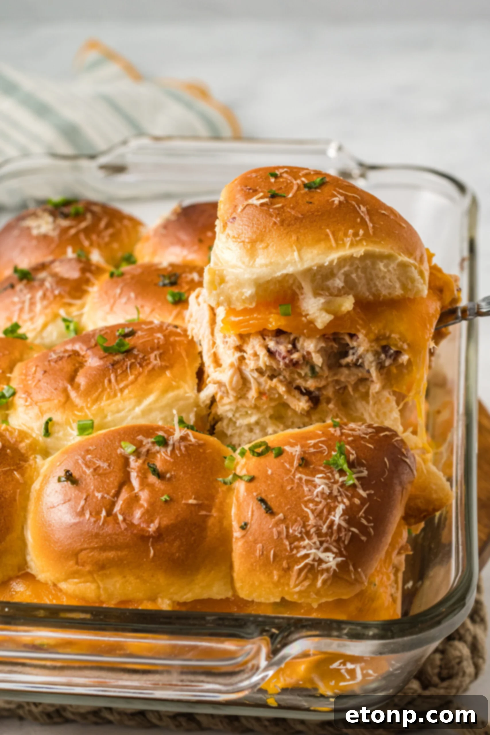 Side view of Crack Chicken Sliders in a clear baking dish with one being lifted by a silver utensil.