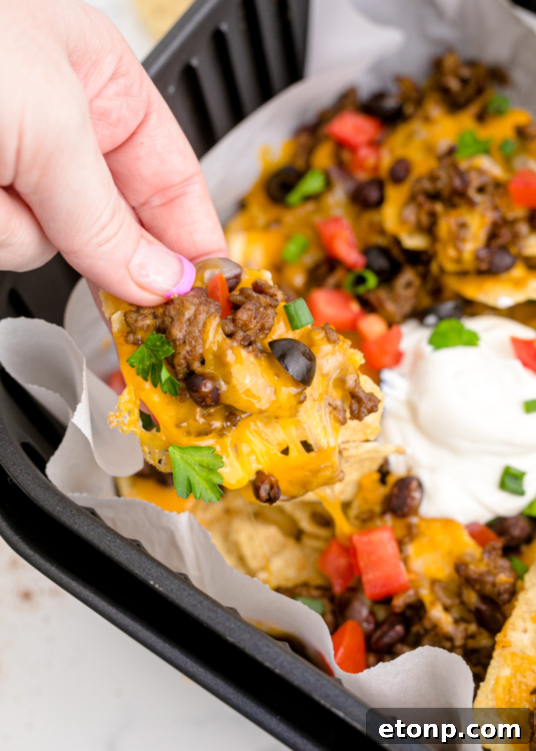 Up close view of Air Fryer Nachos in an air fryer basket and one nacho being held.