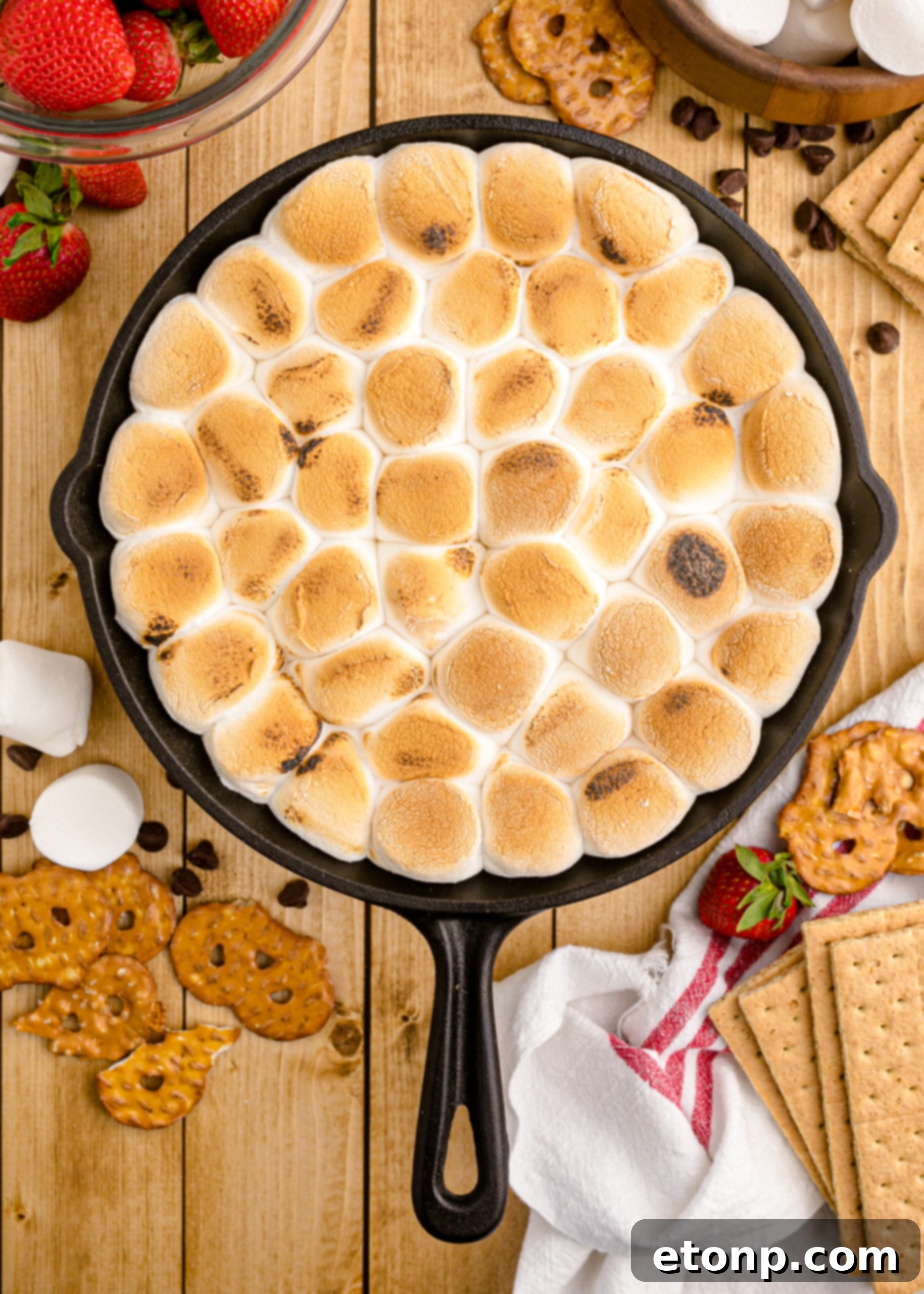 An inviting overhead view of a freshly baked S’mores Dip, bubbling with melted chocolate and golden-brown marshmallows in a rustic cast-iron skillet, ready to be scooped.