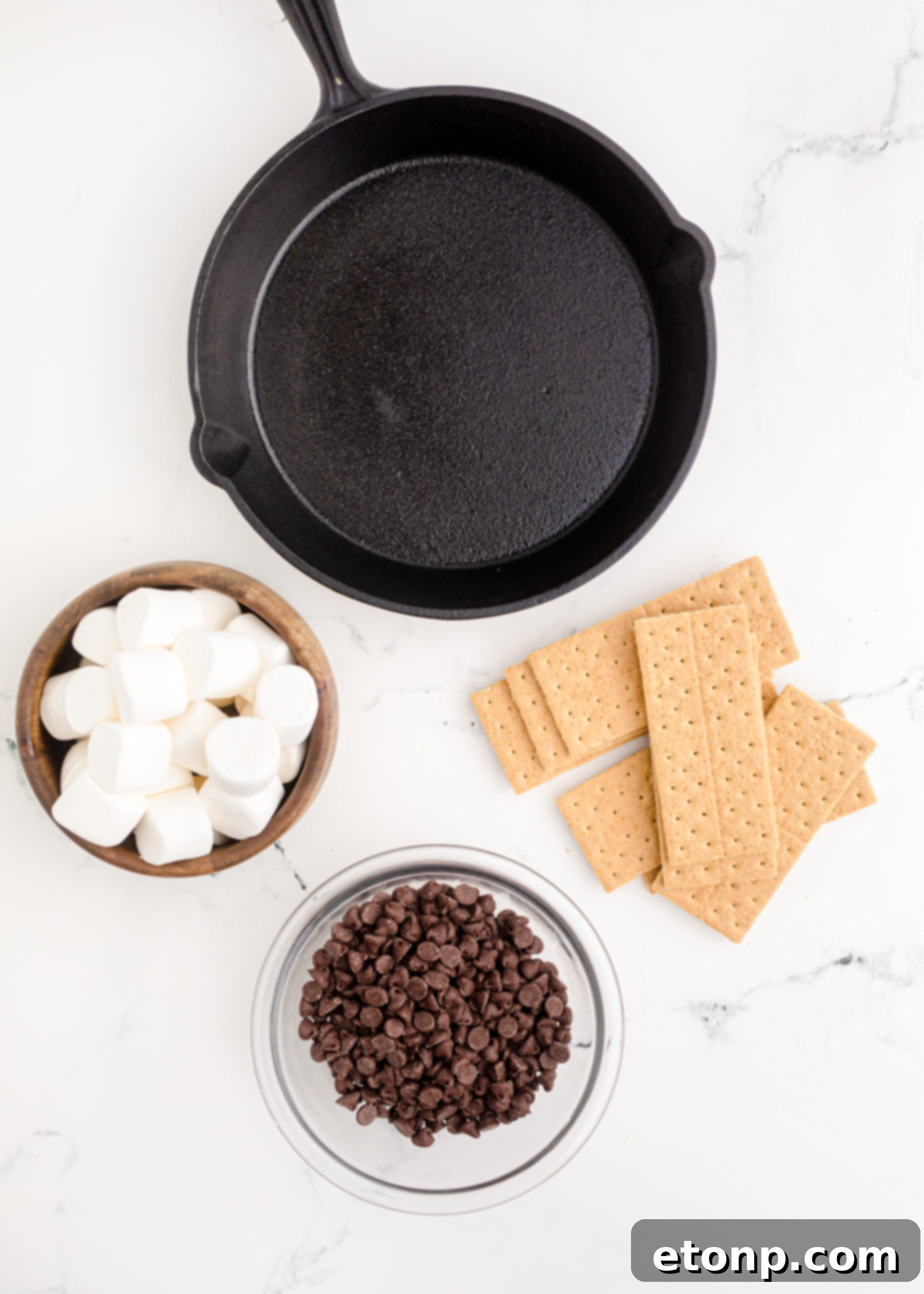 An overhead layout of the three simple ingredients – chocolate chips, a bag of marshmallows, and graham crackers – neatly arranged, ready for the S’mores Dip recipe.