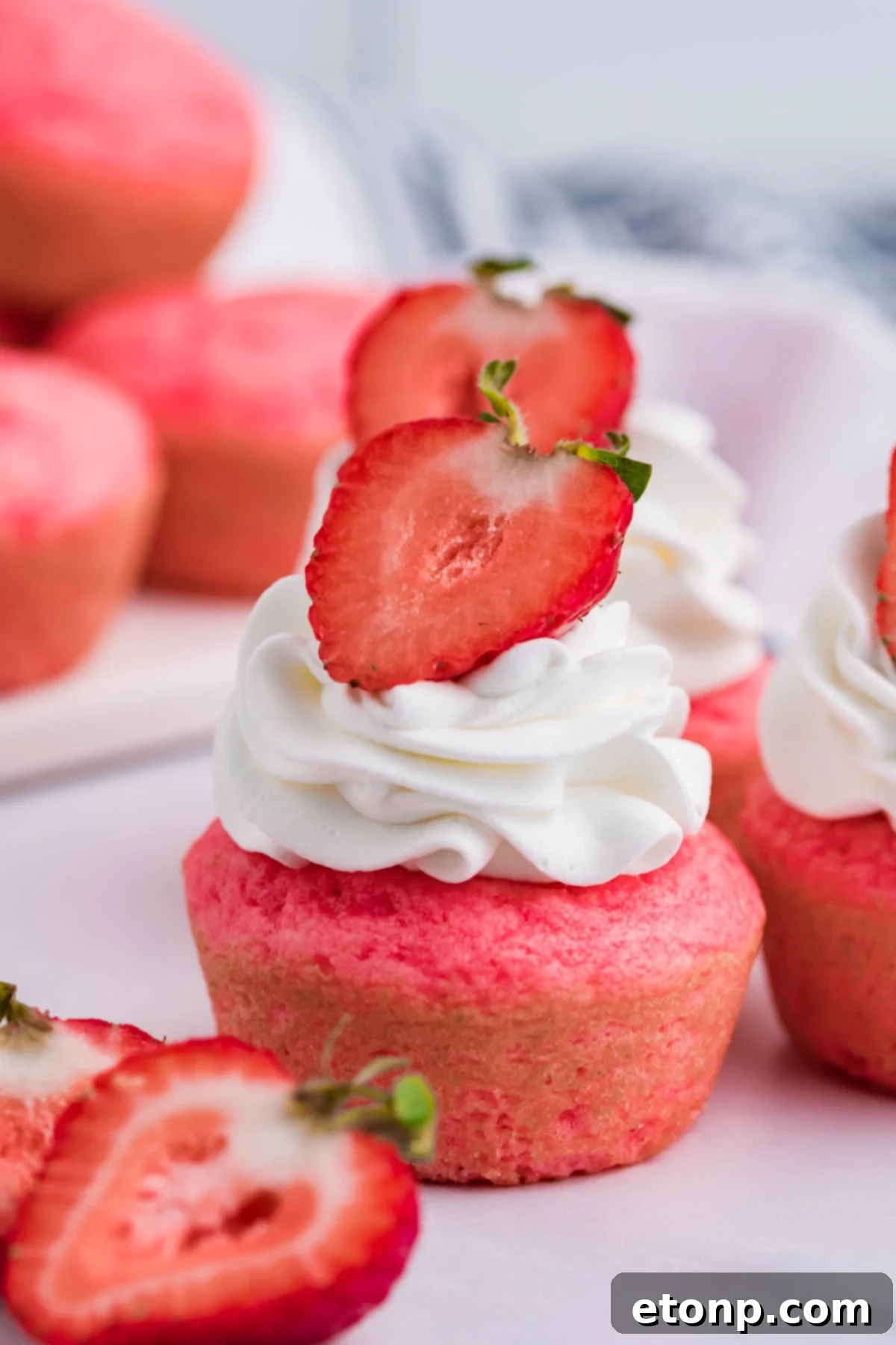 Weight Watchers Strawberry Muffin topped with a swirl of light whipped cream and a fresh strawberry half, set against a bright, inviting background.