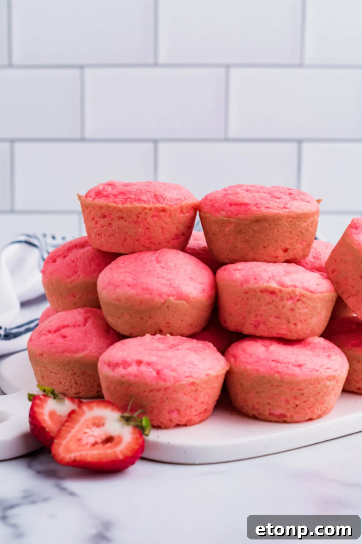 A perfectly arranged stack of three fluffy Weight Watchers Strawberry Muffins on a clean white cutting board, highlighting their golden-brown tops and moist interior.