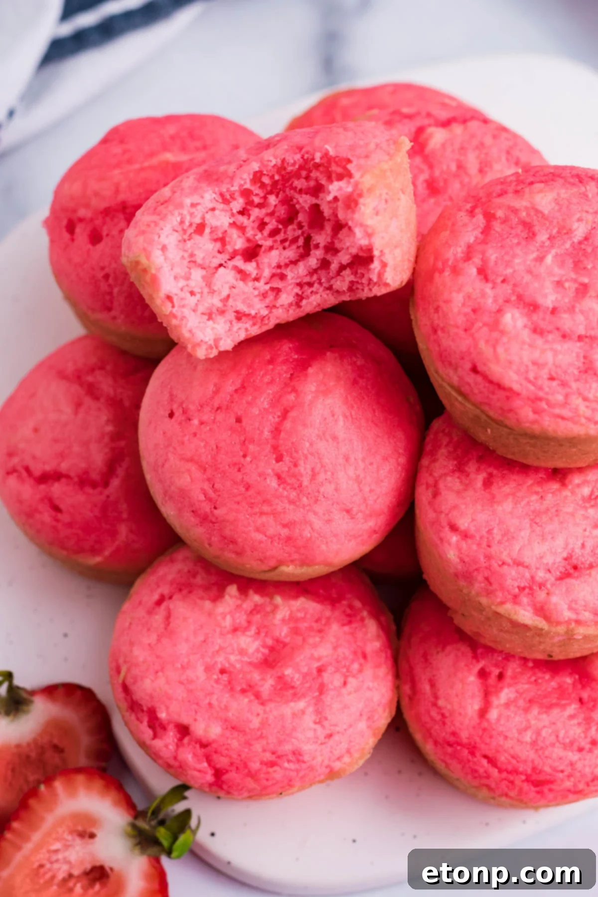 An overhead shot showcasing a stack of homemade Weight Watchers Strawberry Muffins on a white cutting board, with one muffin playfully missing a bite, revealing its soft texture.