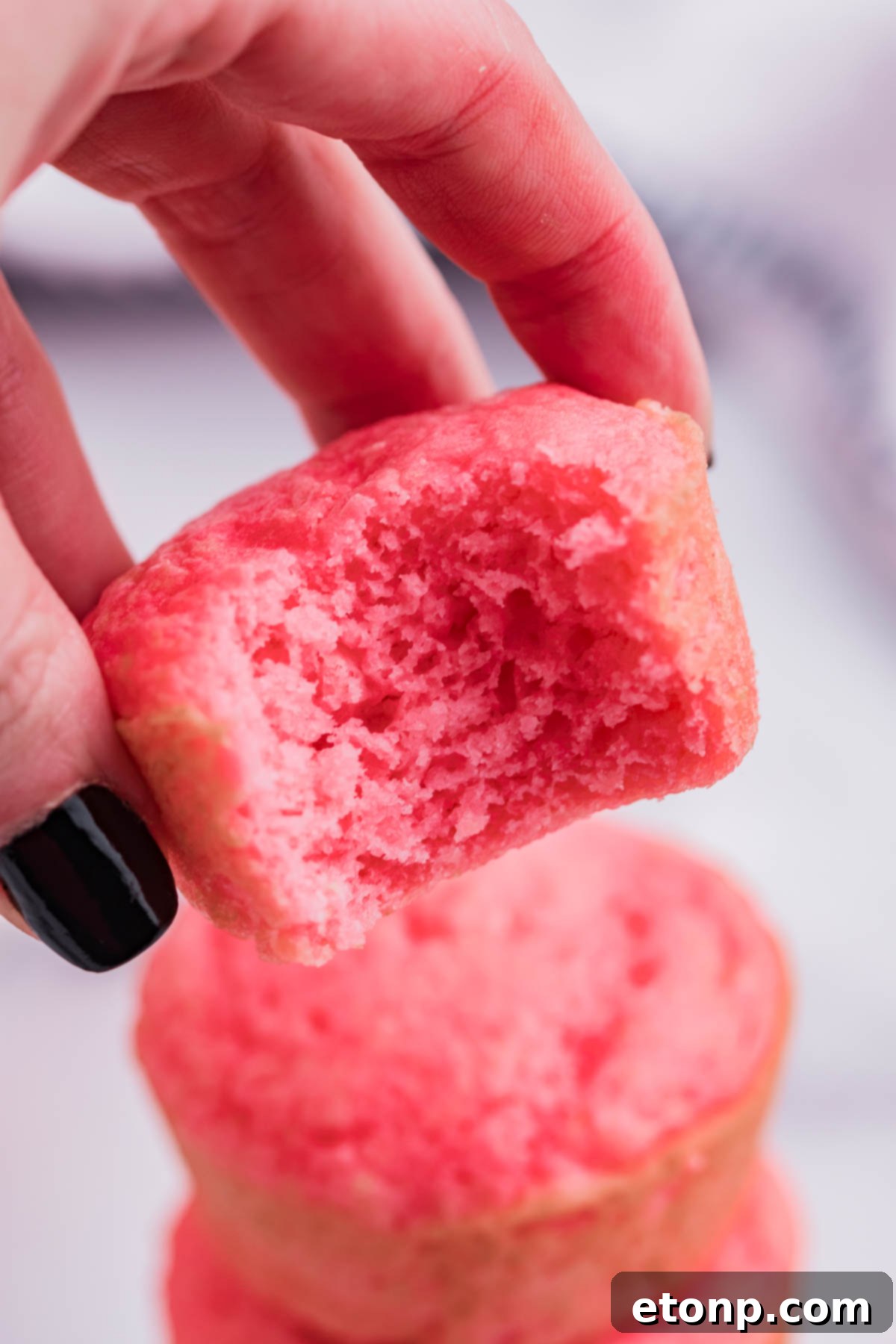 An inviting close-up of a single Weight Watchers Strawberry Muffin with a perfect bite removed, highlighting its airy texture and the visible strawberry pieces within.