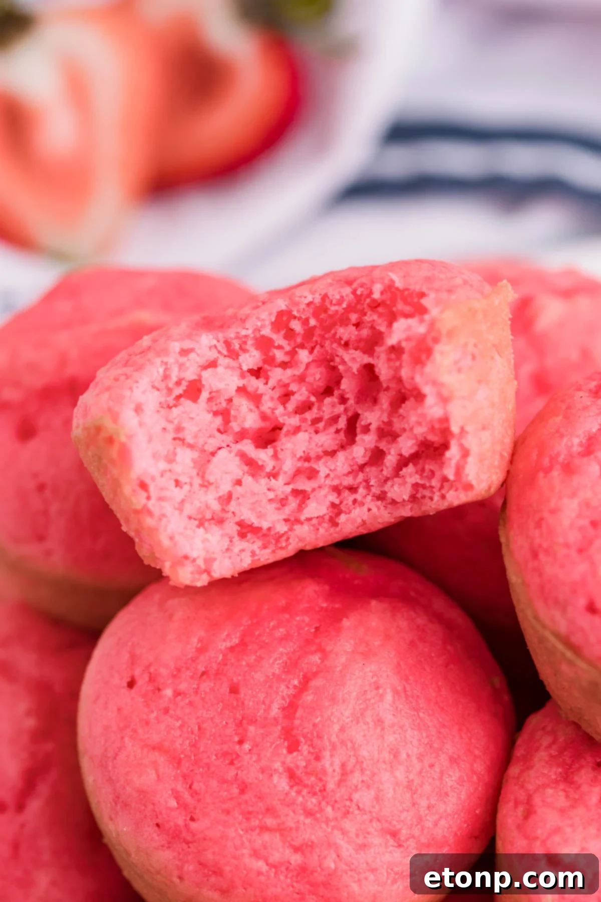 A close-up view of a stack of Weight Watchers Strawberry Muffins on a white cutting board, with a bite taken out, highlighting the moist texture and healthy appeal.