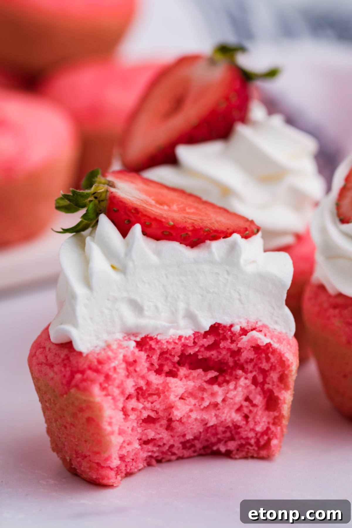 A single Weight Watchers Strawberry Muffin, beautifully adorned with whipped cream and a strawberry half, with a portion already enjoyed, emphasizing its delightful taste.