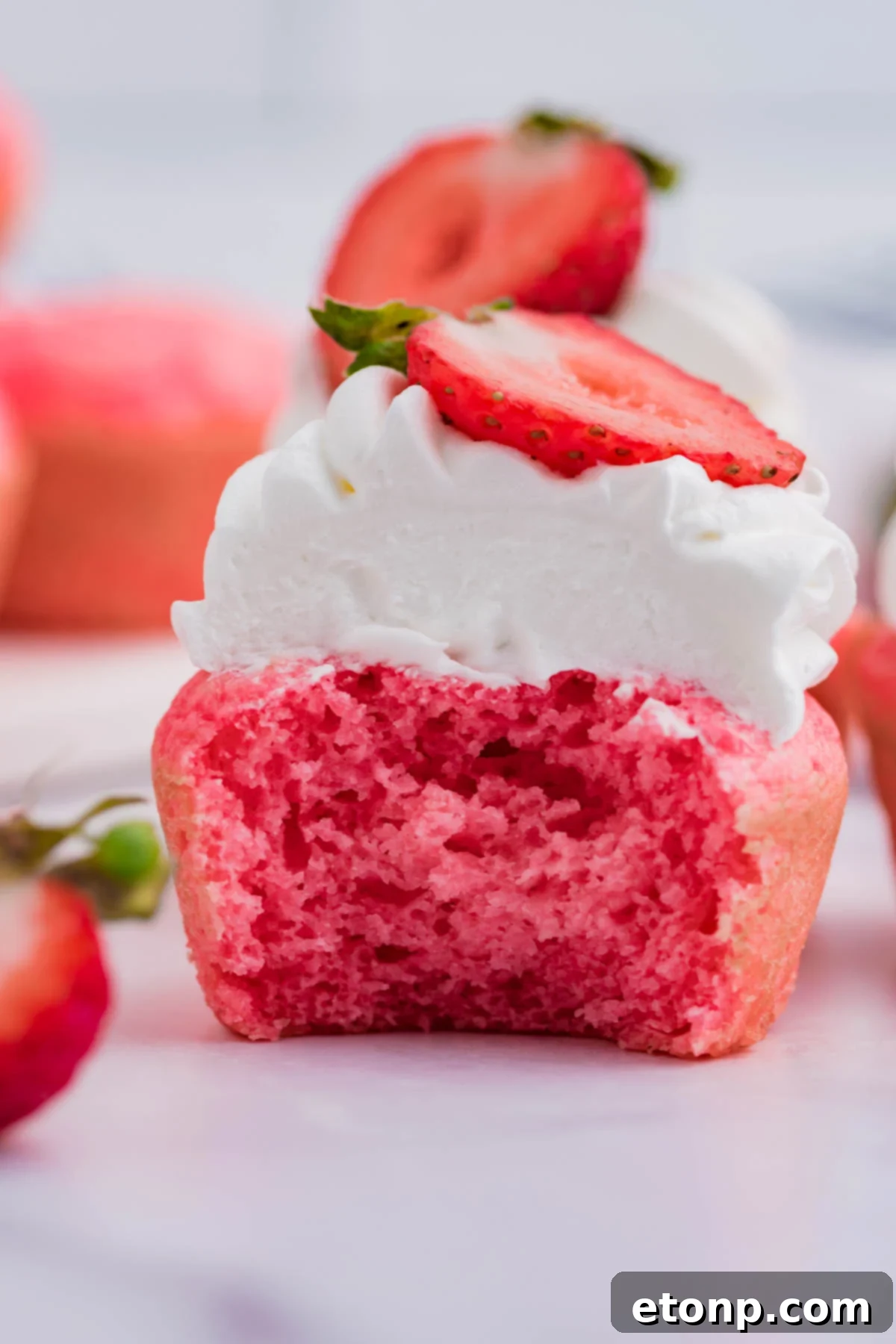 An identical view of a Weight Watchers Strawberry Muffin, topped with whipped cream and a strawberry half, half-eaten to highlight its appealing texture and taste.