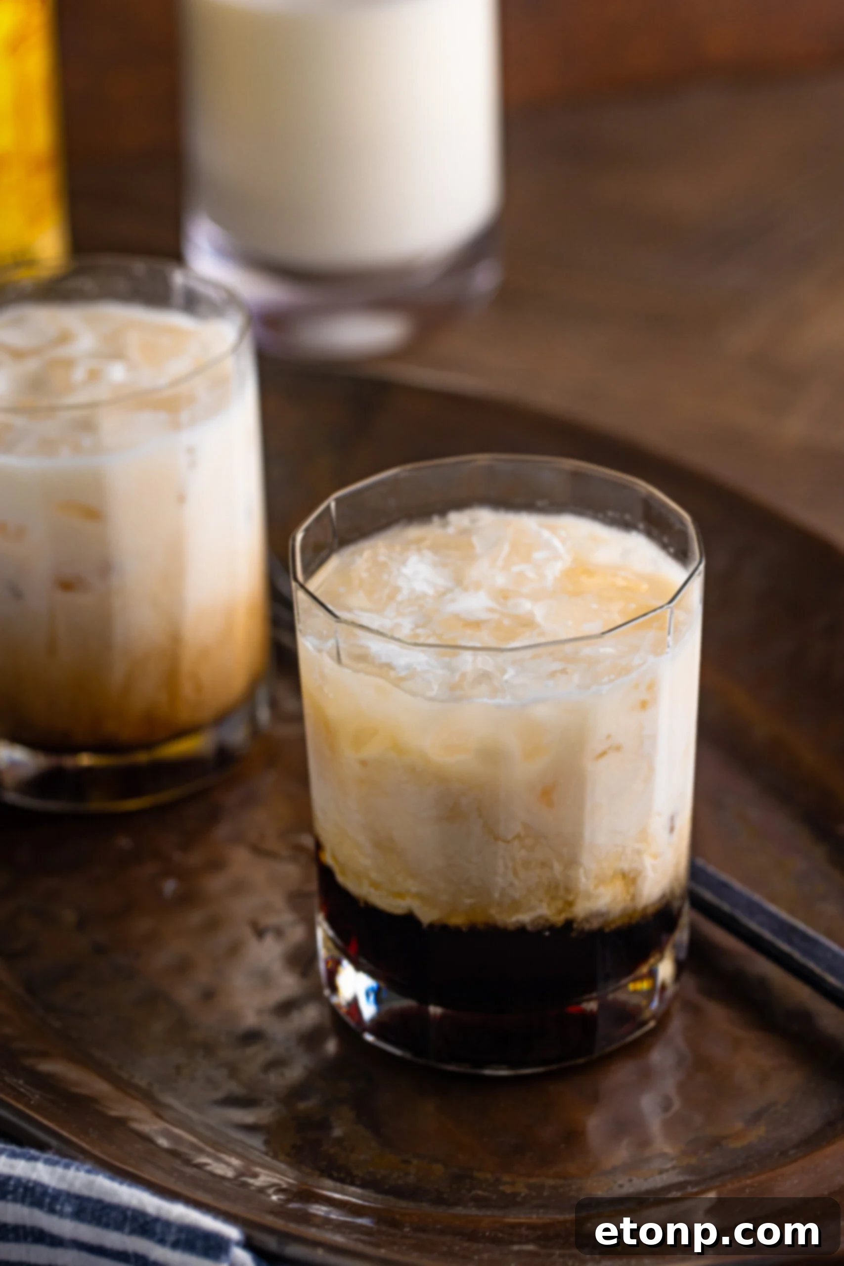 White Russian in a clear glass sitting on a dark metal serving tray, highlighting its inviting color.