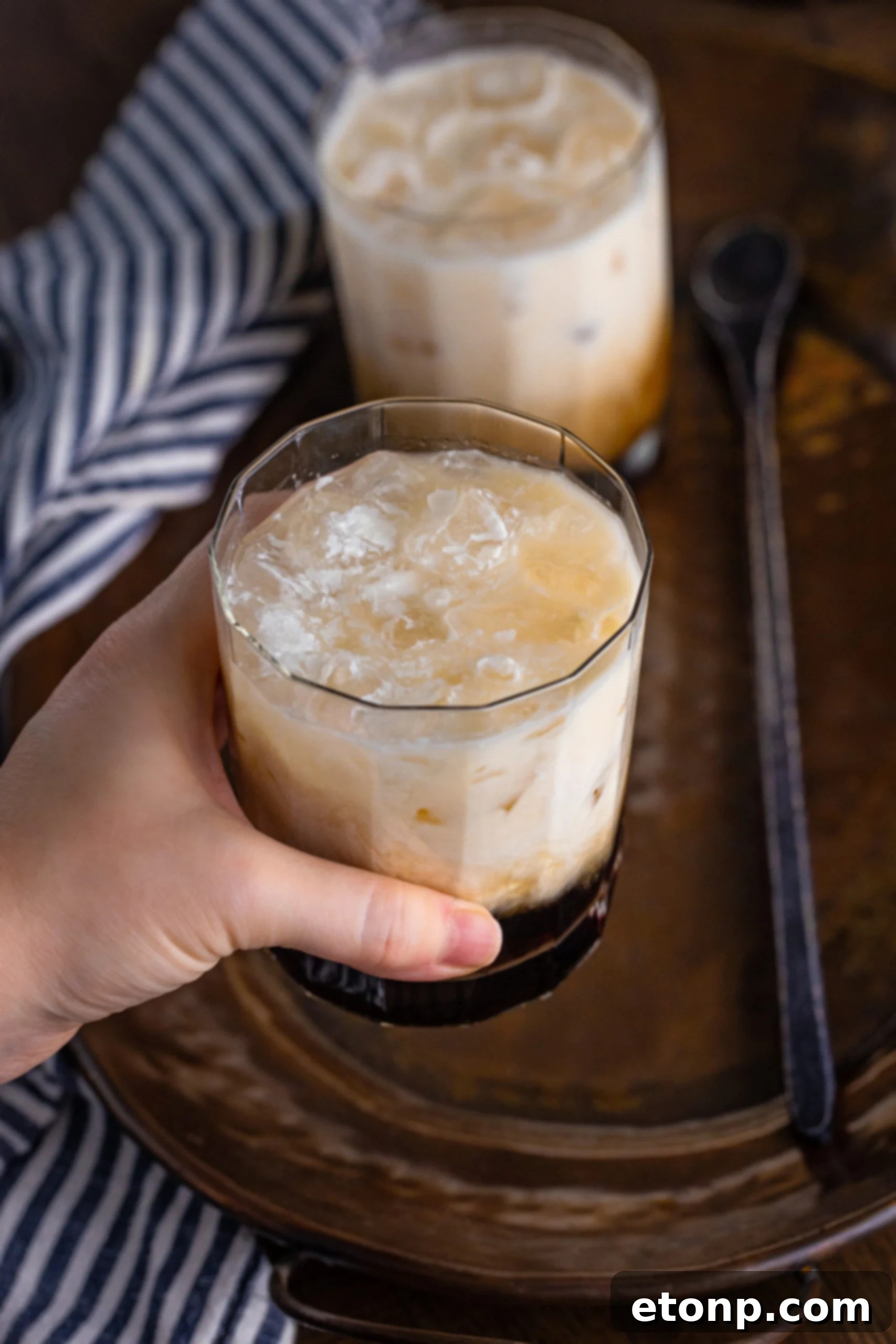 A hand holding a White Russian drink in a clear glass, perfect for a relaxing moment.