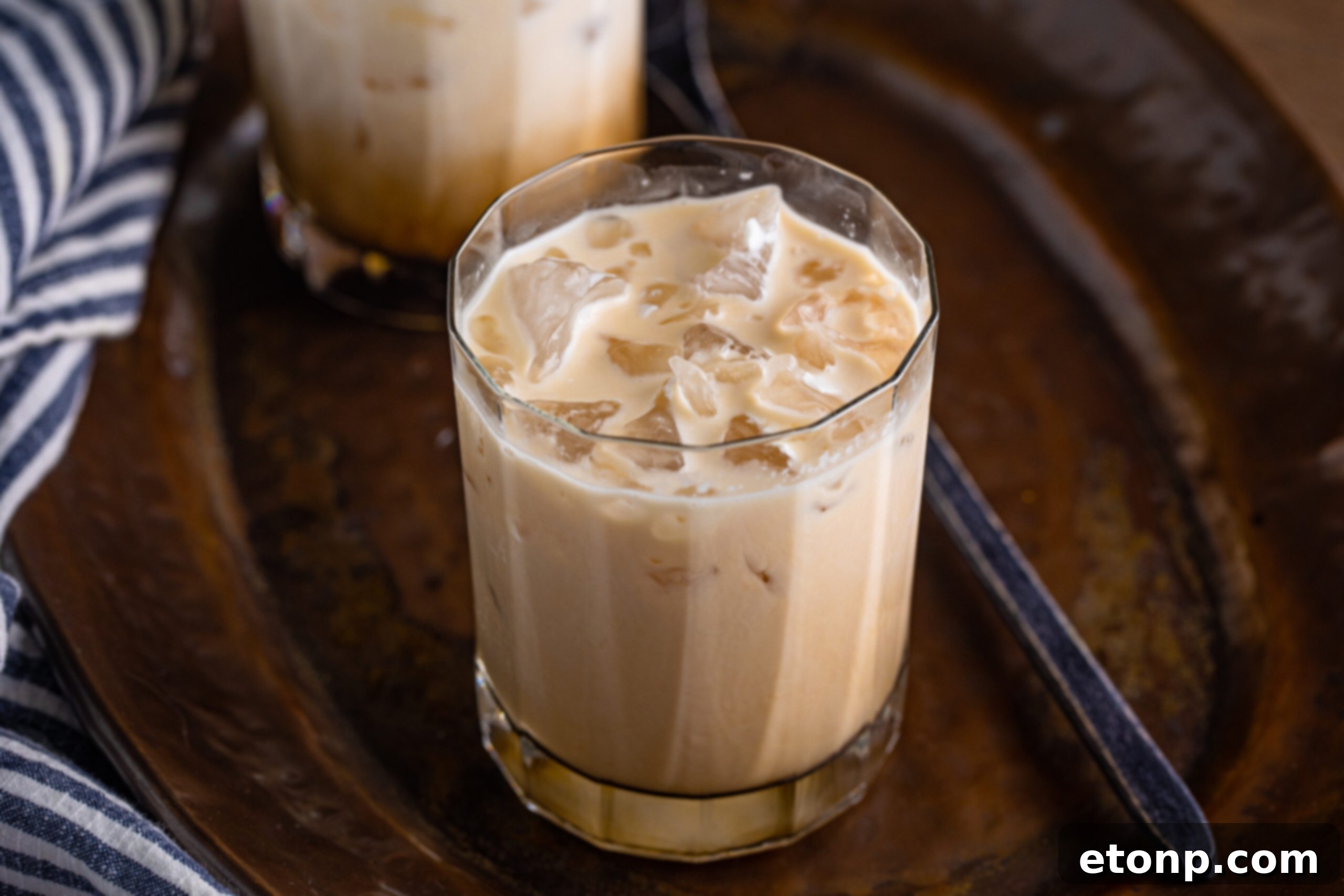 White Russian cocktail mixed in a clear glass, placed on a dark metal serving tray, highlighting its rich color.