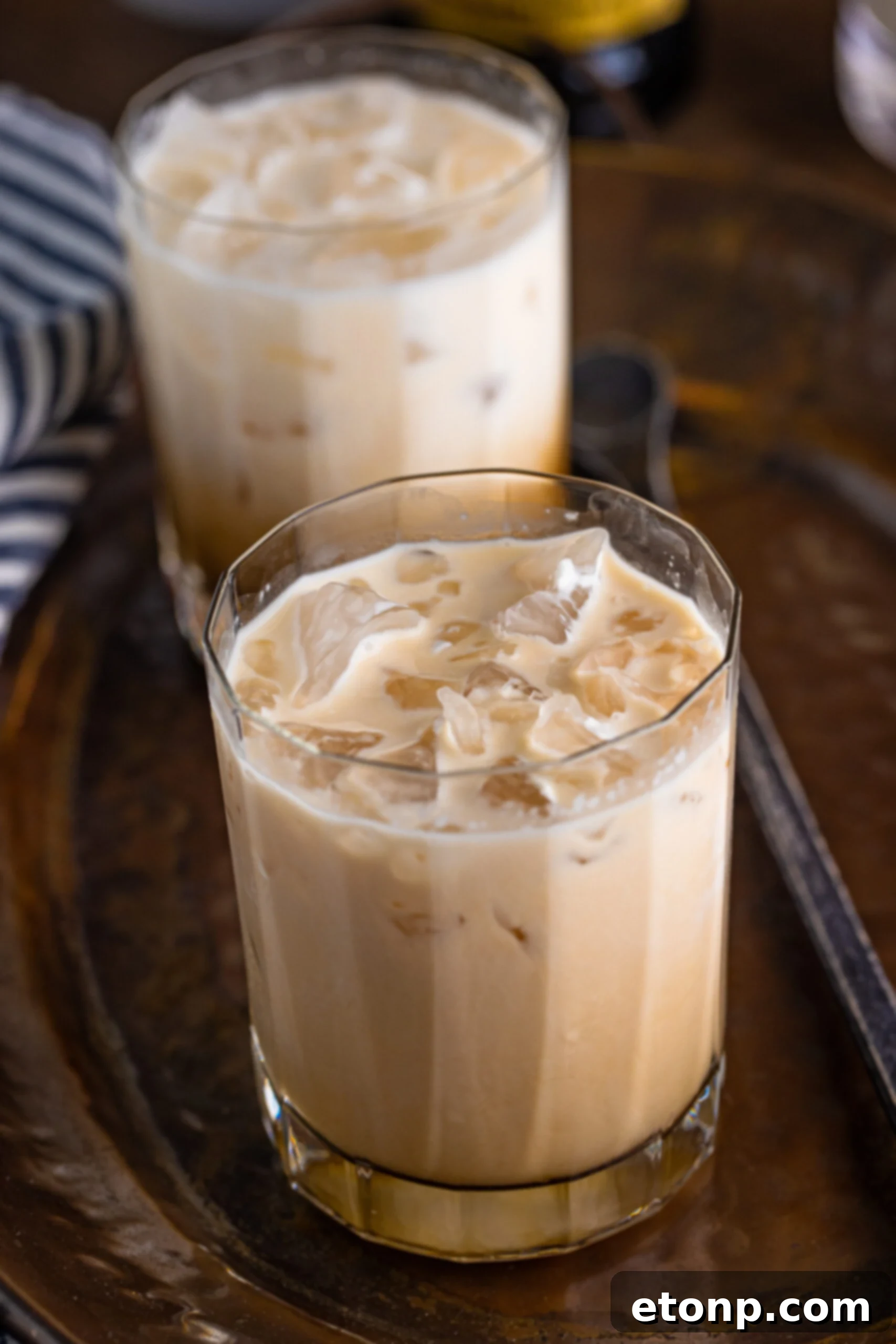 A White Russian cocktail, perfectly mixed, in a clear glass on a dark metal serving tray, showcasing its appealing visual texture.