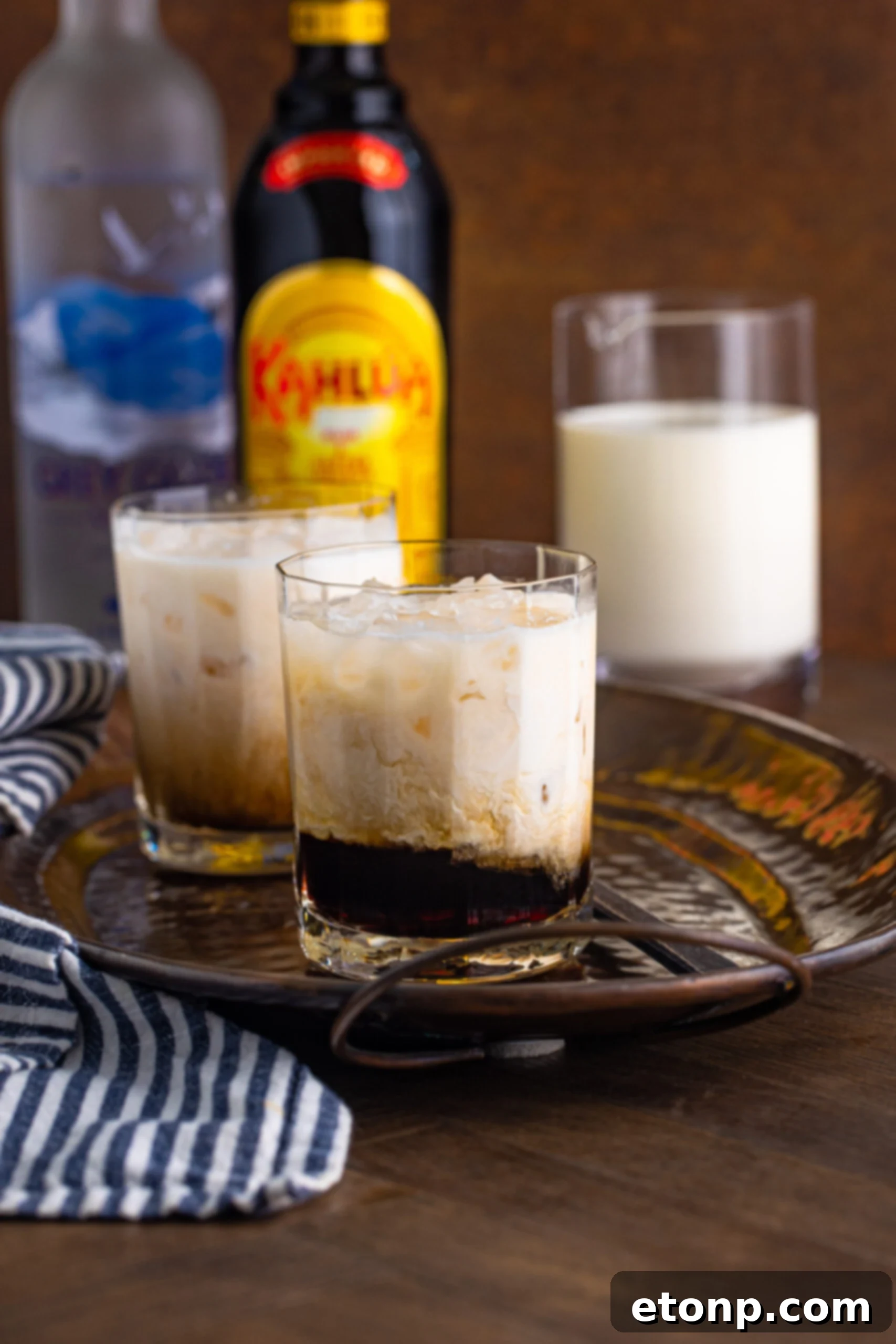 White Russian in a clear glass sitting on a dark metal serving tray, ready to be enjoyed.